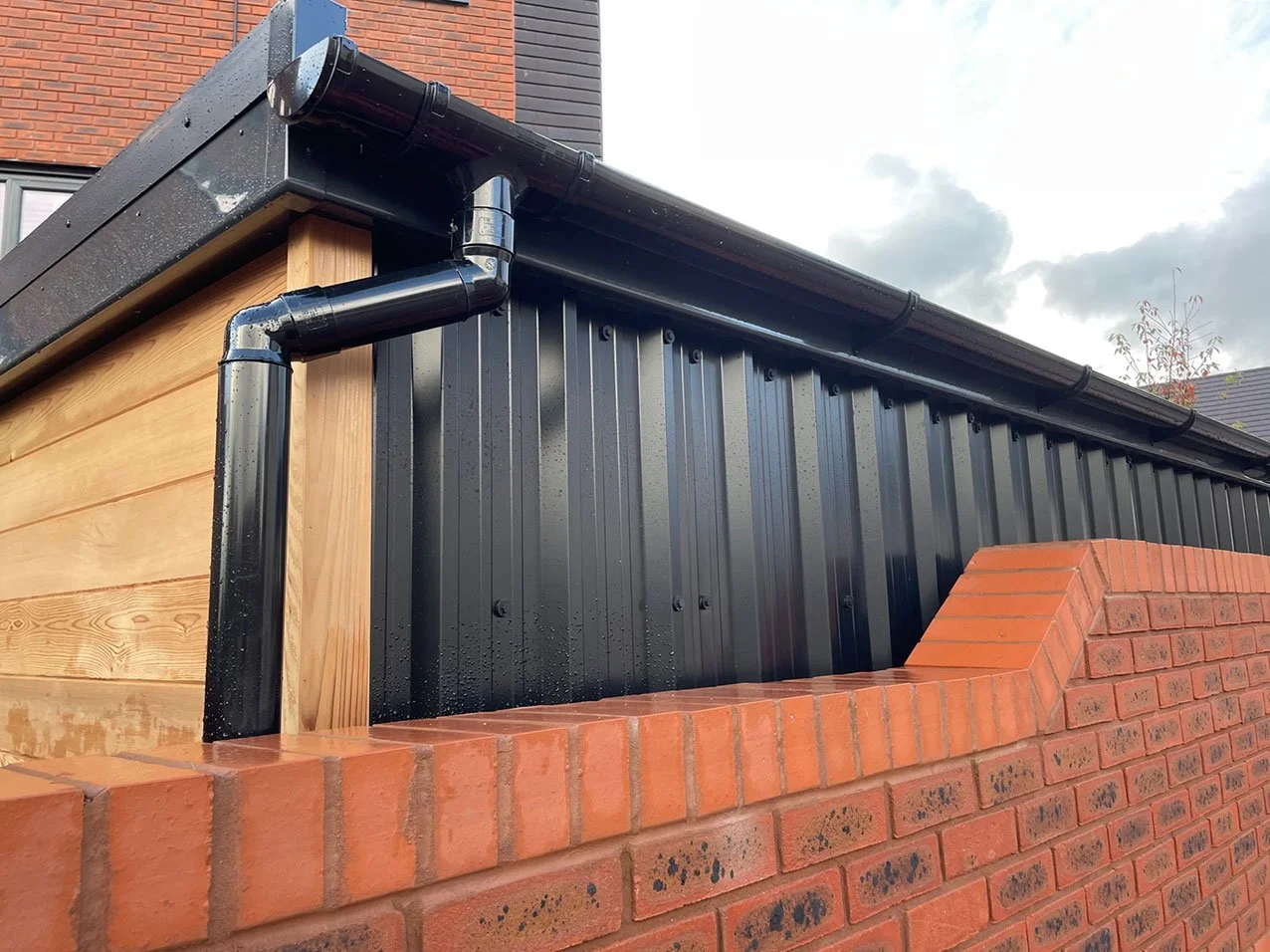  This picture depicts a brick wall accompanied by a black metal roof and a pipe, exemplifying a solid and functional design. 