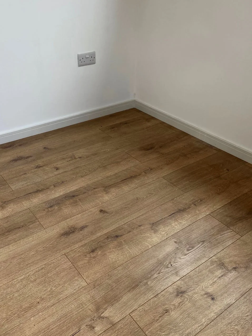 An interior space featuring polished wood flooring and a clean white wall. 