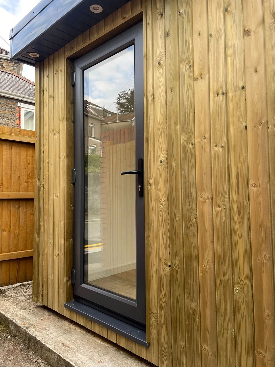  A quaint wooden garden office with a sliding door and surrounding wooden fence. 