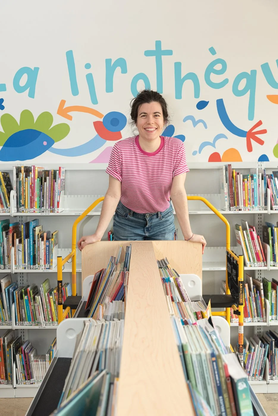 Portrait de Elbé posant devant sa murale pour la bibliotheque de l'école Notre-Dame-du-Canada