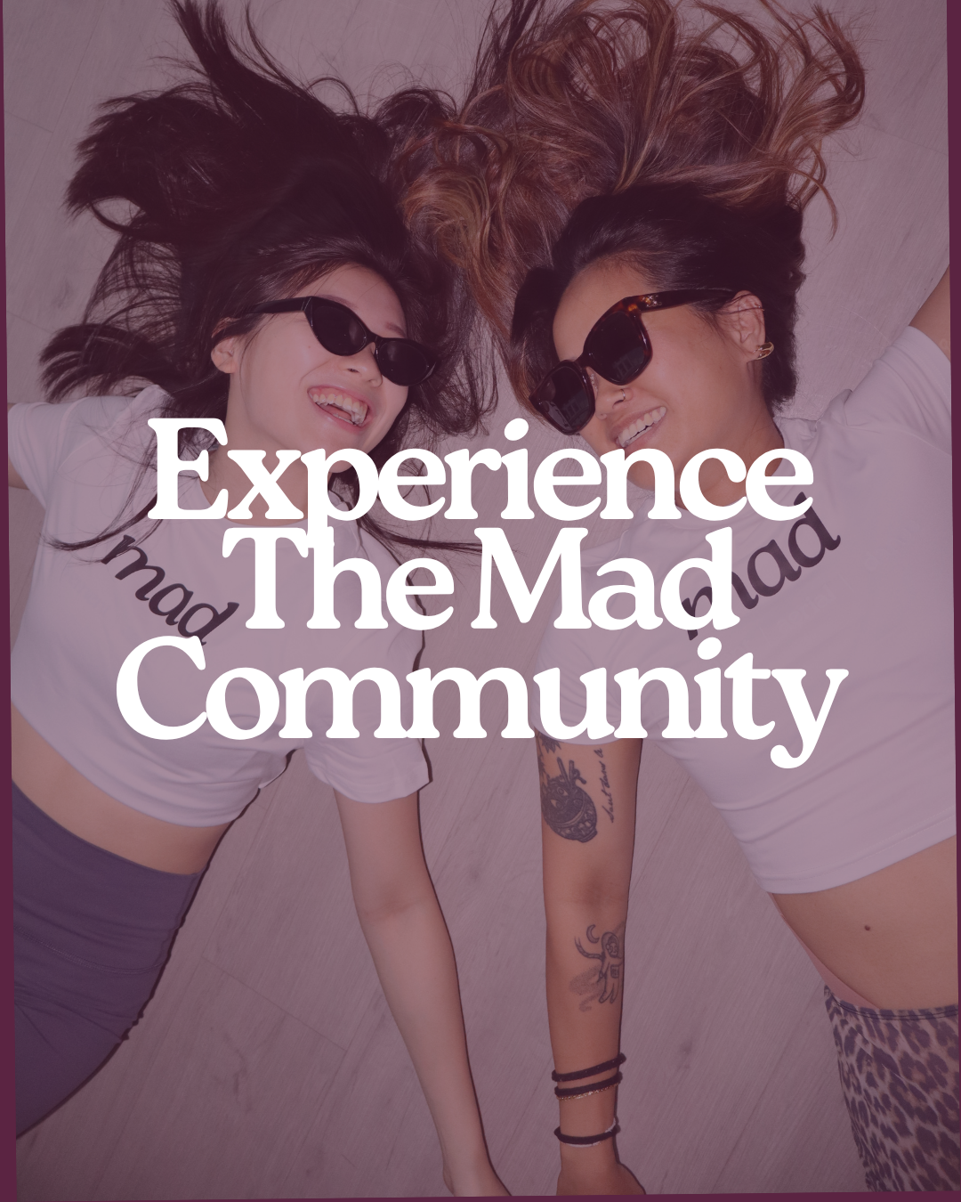 Two women with long hair lying on the floor, smiling, wearing sunglasses and t-shirts with text, with the overlay text 'Experience The Mad Community'.