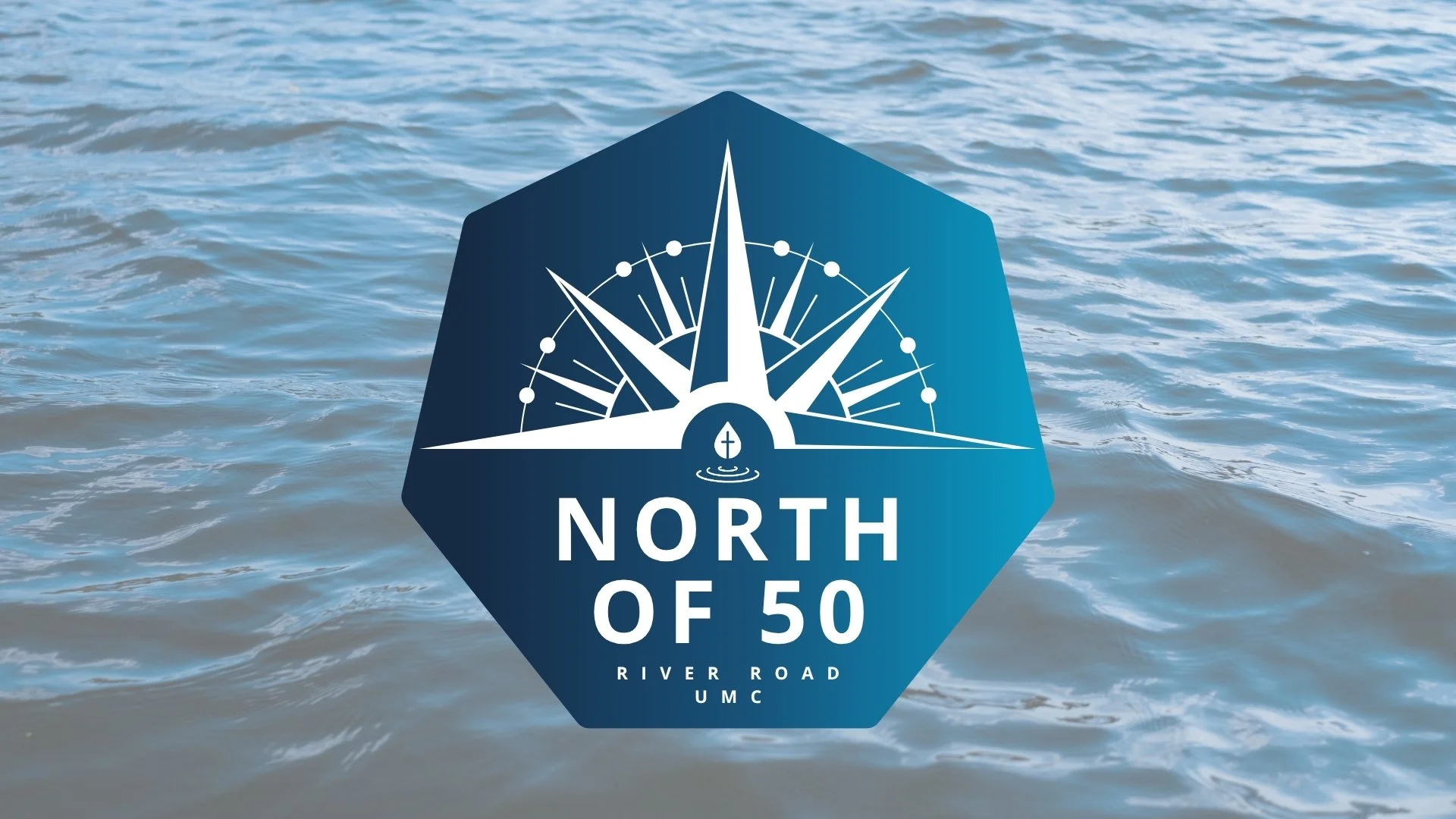 A blue octagonal sign with a white compass graphic and a small sailboat icon, displaying the text 'North of 50 River Road UMC' over water.