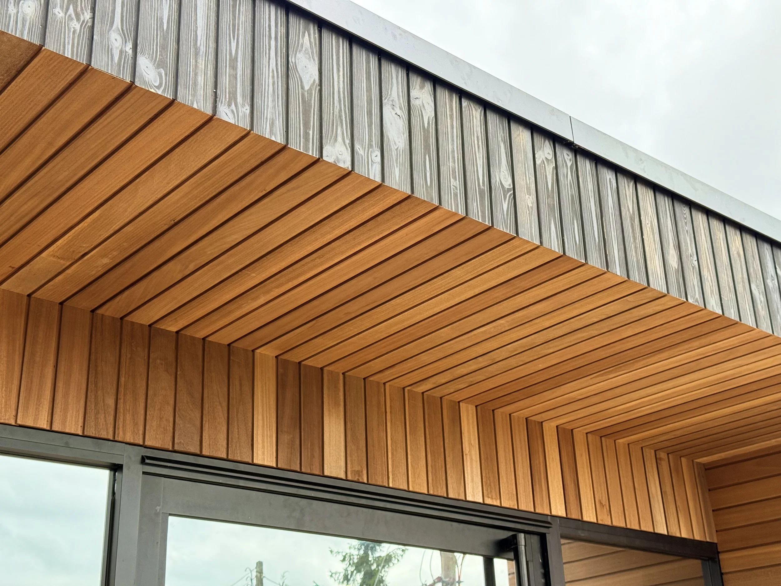 Close-up view of modern building exterior with wooden paneling and metal framing, sky visible in background.