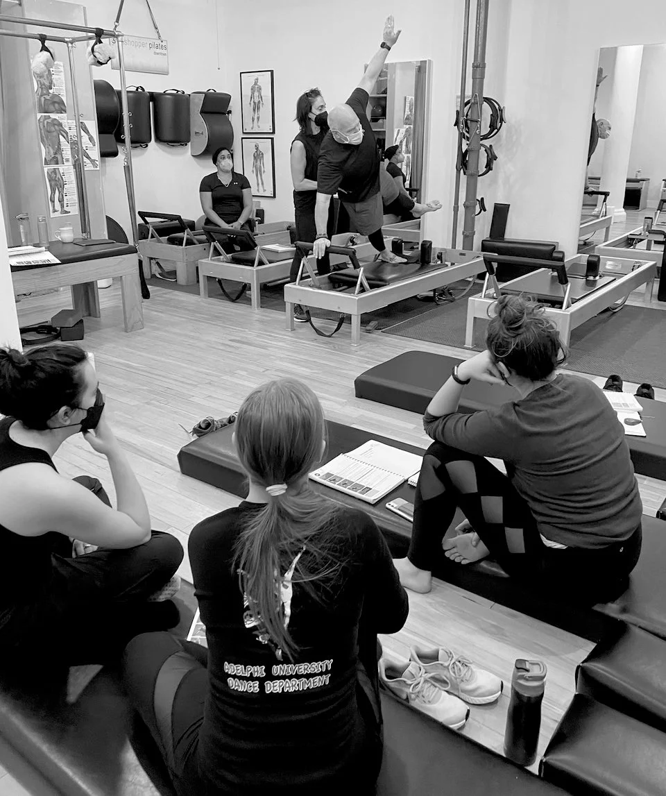 People attending a Teacher Training Course with an instructor demonstrating exercises on a reformer machine in a Classical Pilates studio.