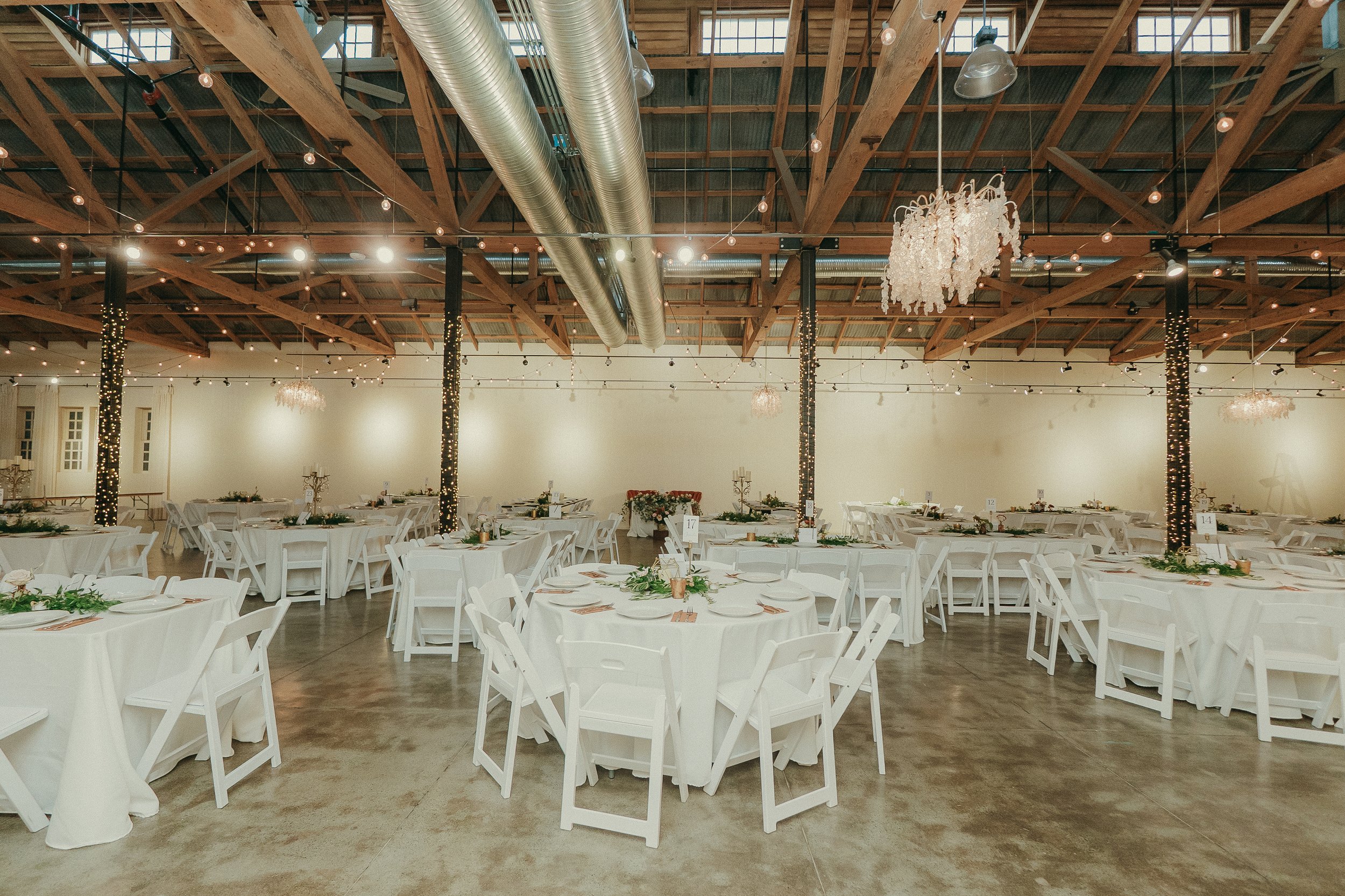 The Ballroom at The Westport | Downtown Chico: A premier indoor wedding ceremony space featuring authentic historic beams, romantic string lighting, and our iconic reclaimed tin barn door. 12,000 square feet of versatile, industrial elegance for your