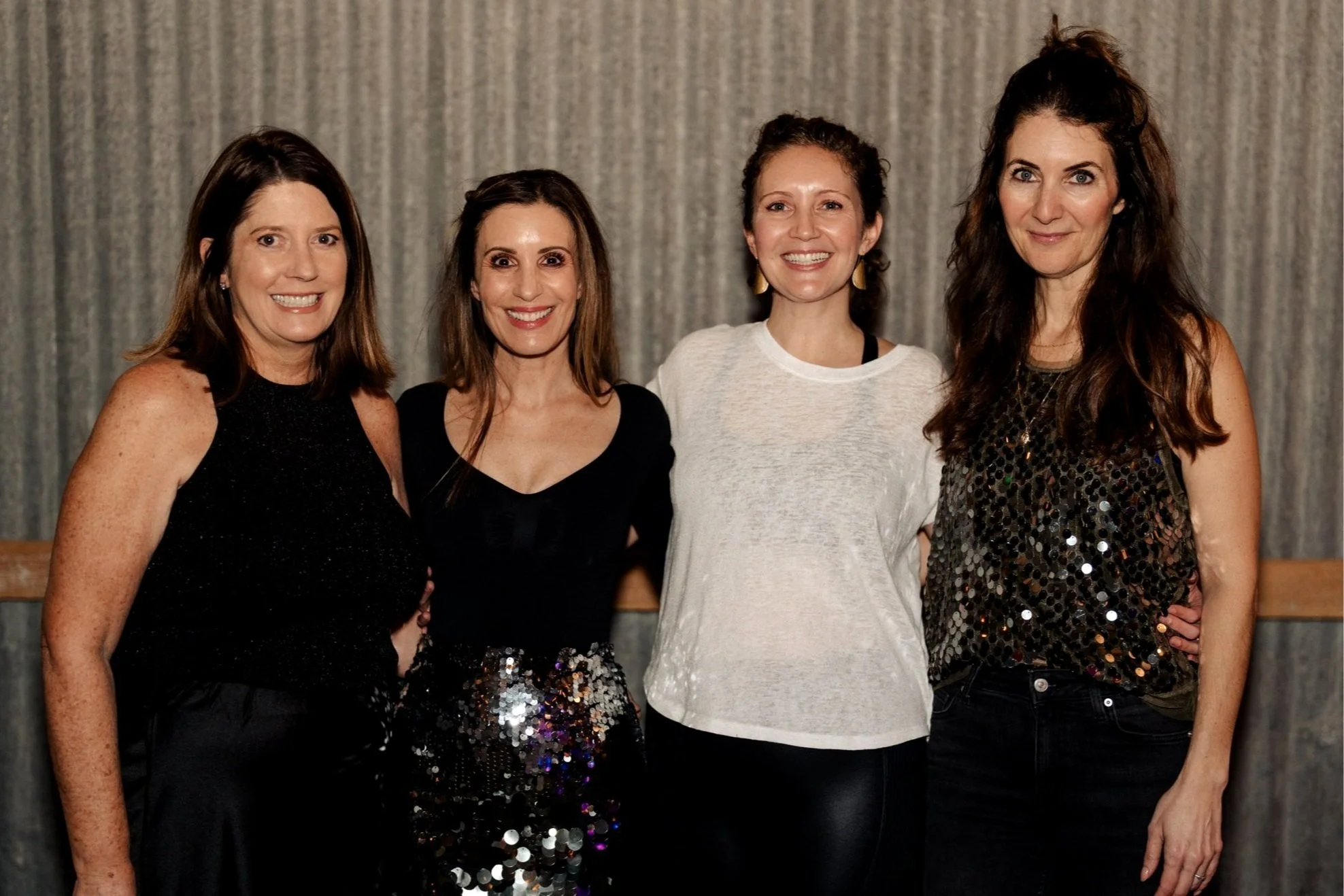 Four owners standing close together, smiling at the camera, in front of a curtain backdrop.