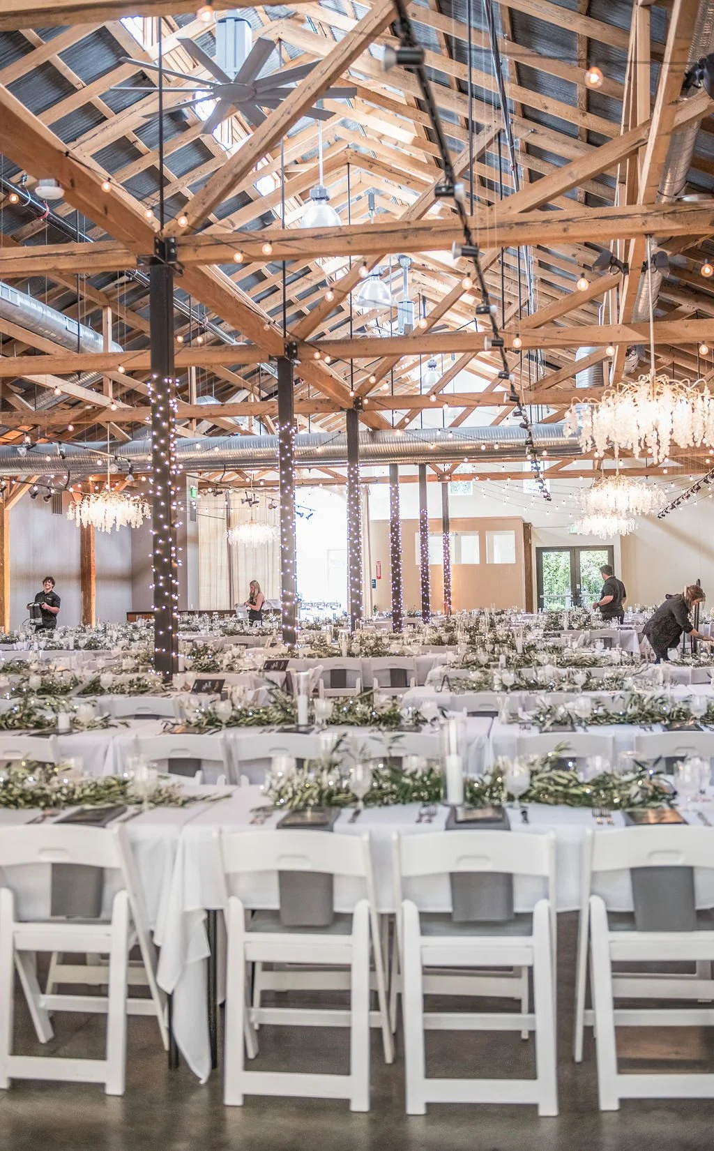 tables set for a gala with white linens and caterers filling water glasses in the glowing ballroom at the westport in downtown chico ca