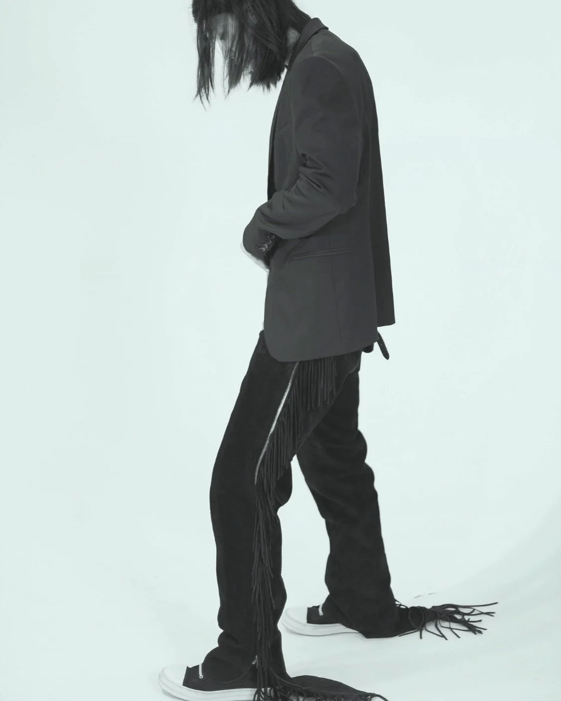 Person wearing a blazer with fringe pants and sneakers, standing against a light background.