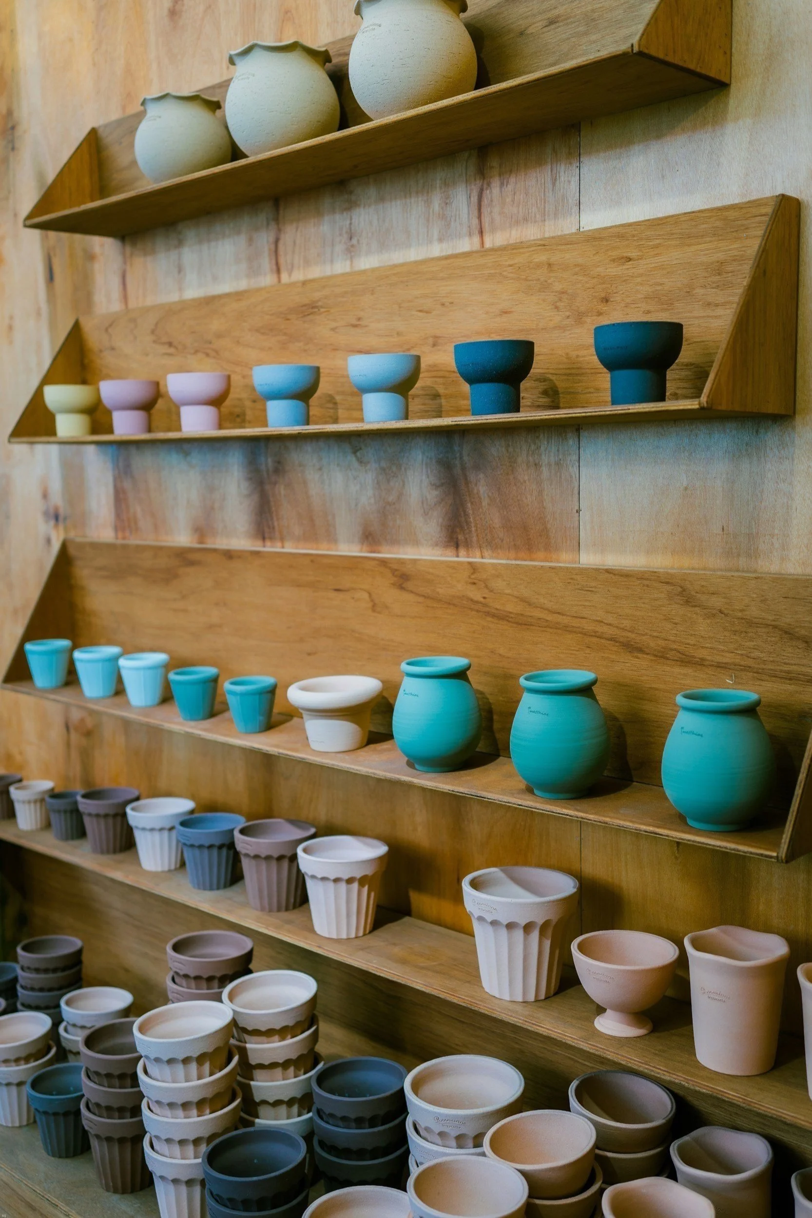 Shelves filled with colorful pottery cups and small vases, arranged in rows, on a wooden display wall.