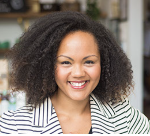 Smiling person with curly hair wearing a striped shirt in an indoor setting.