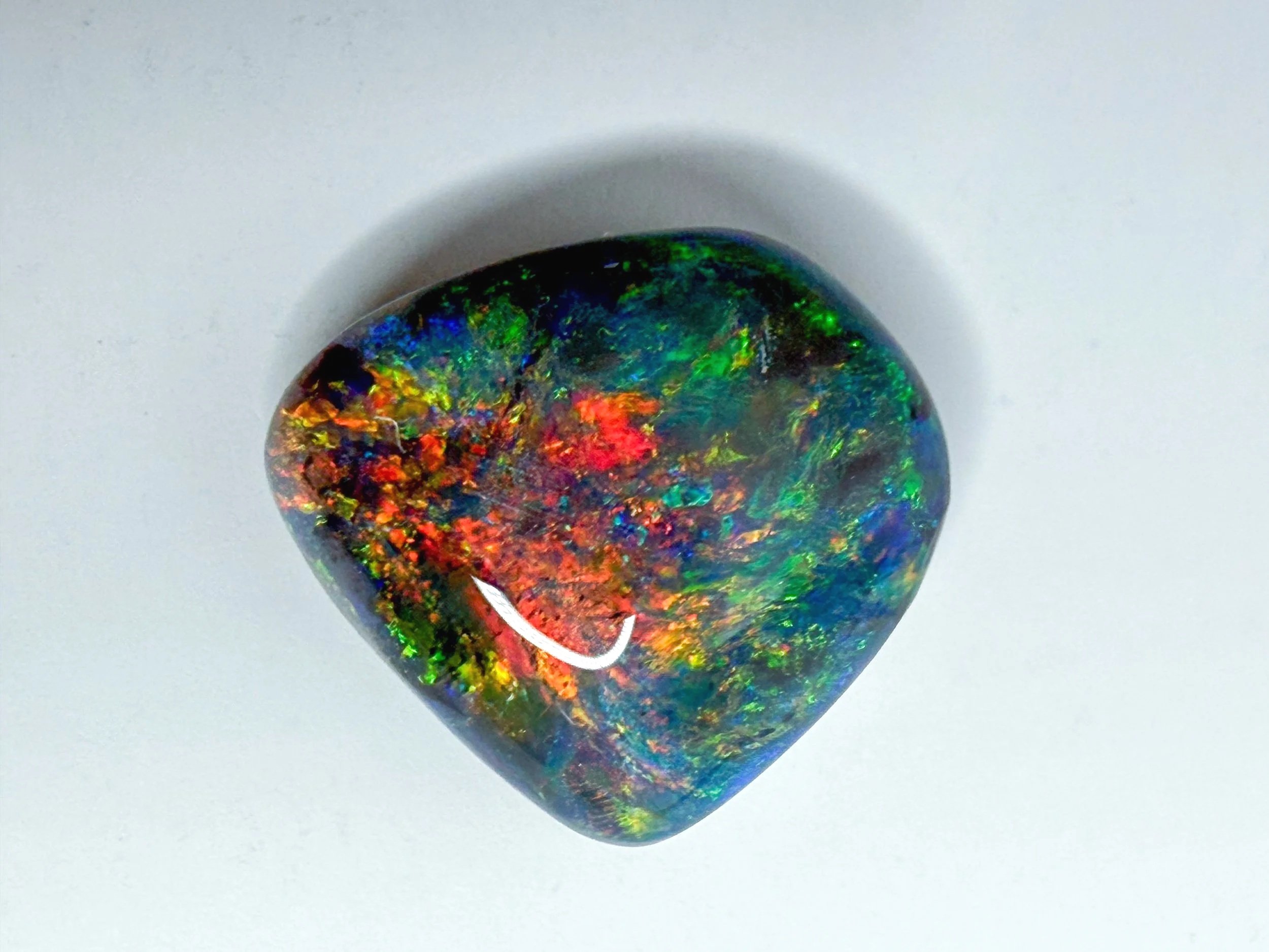 Close-up image of a polished black opal gemstone with vibrant red, green, blue, and yellow colors, cast on a white background.