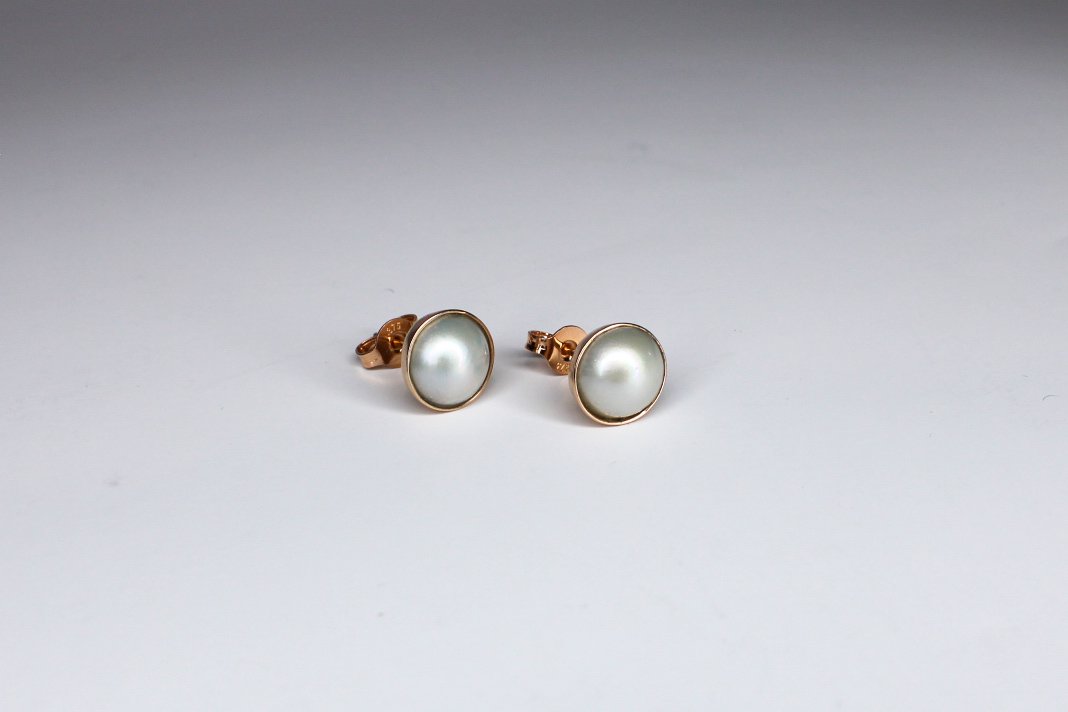 Gold-tone stud earrings with white pearl centers on a plain white background.