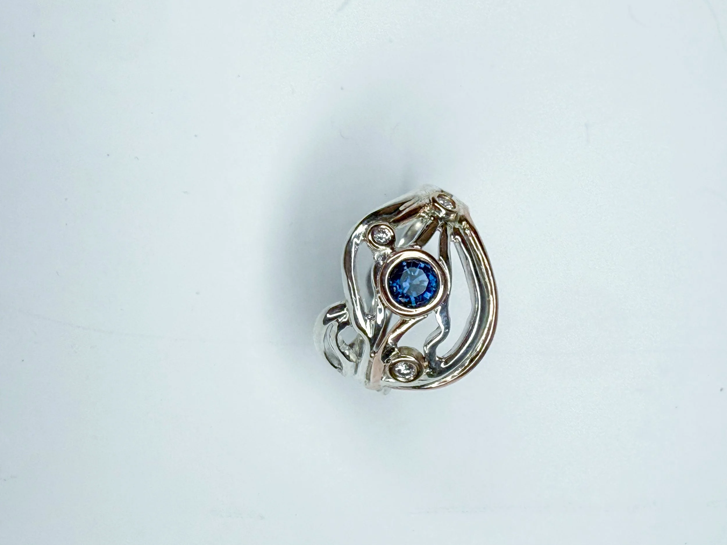 Silver ring with an intricate openwork design and a central blue gemstone, flanked by small clear stones, on a white background.