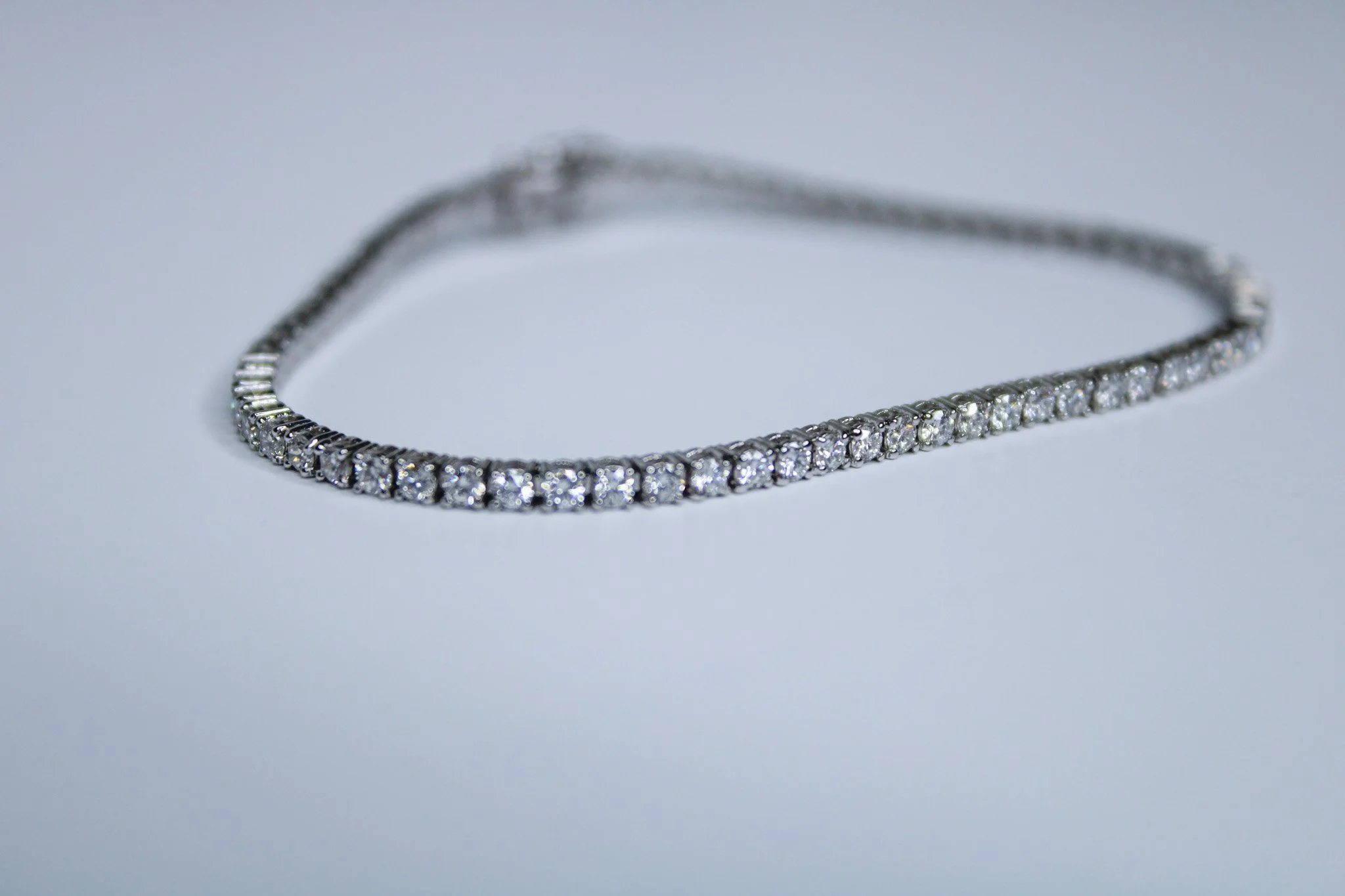 A silver necklace with round-cut diamonds laid out on a white surface.