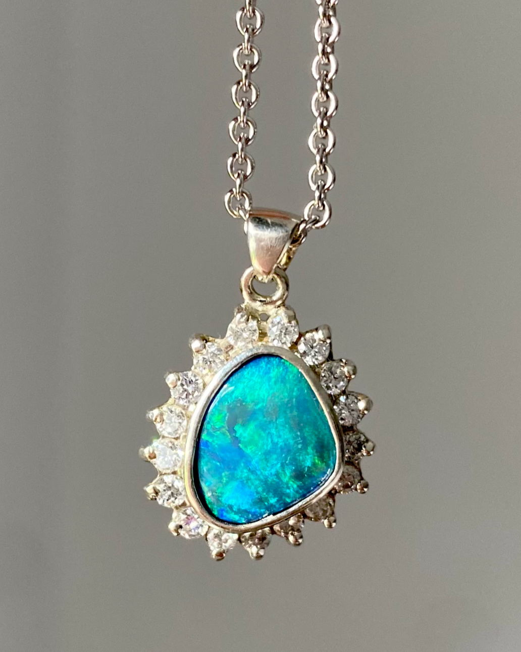 Silver necklace with a large, triangular blue opal pendant surrounded by small clear gemstones.