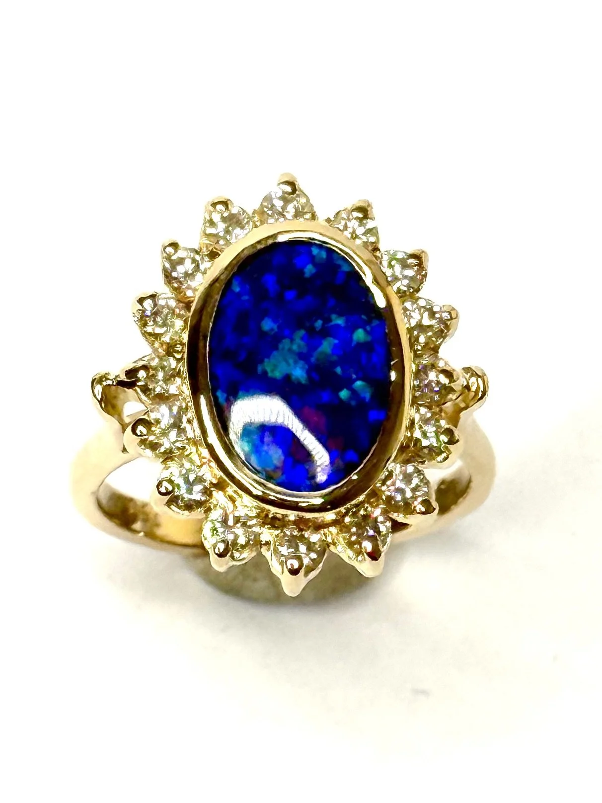 Gold ring with an oval blue stone surrounded by small clear gemstones on a white background.