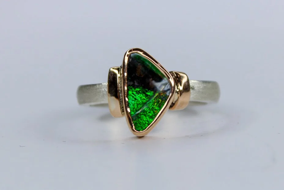 A ring with an asymmetrical triangular green gemstone set in a mixed metal band, with rose gold accents on either side.