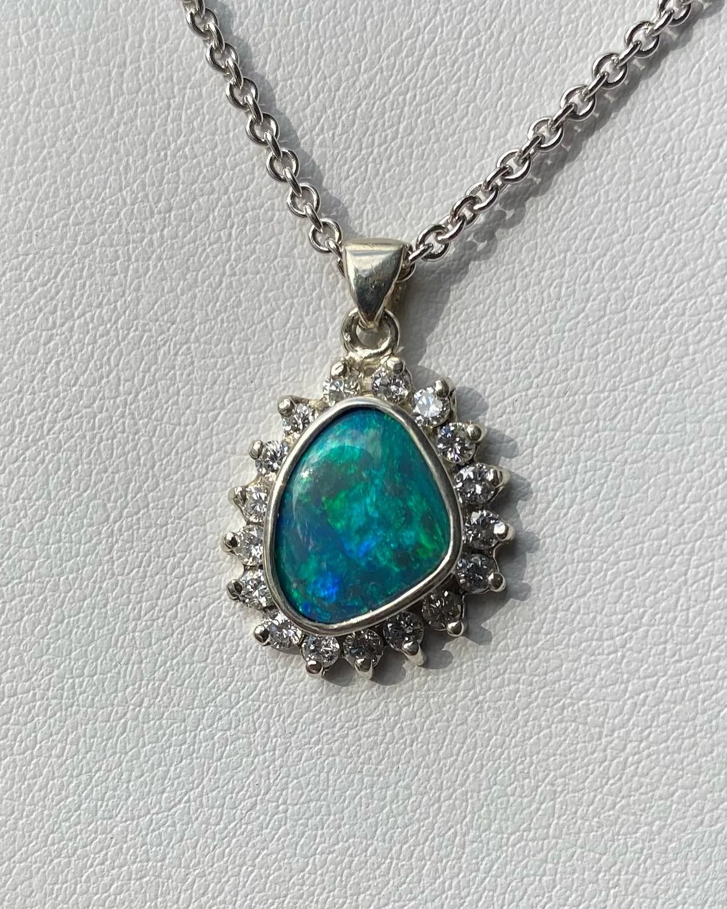 Silver necklace with a teardrop-shaped opal pendant surrounded by small diamonds.