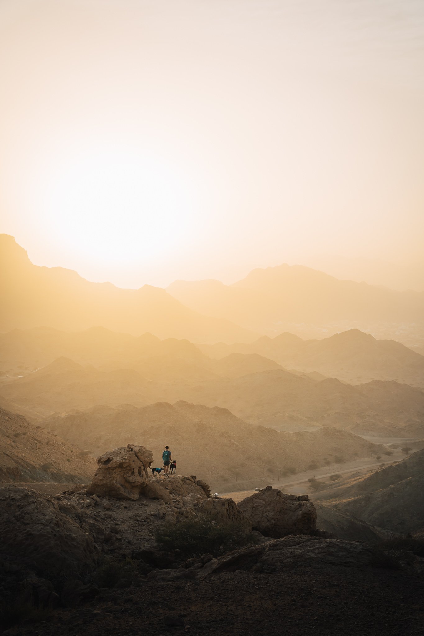 A person hiking in a desert landscape at sunset with mountains and hills in the background.