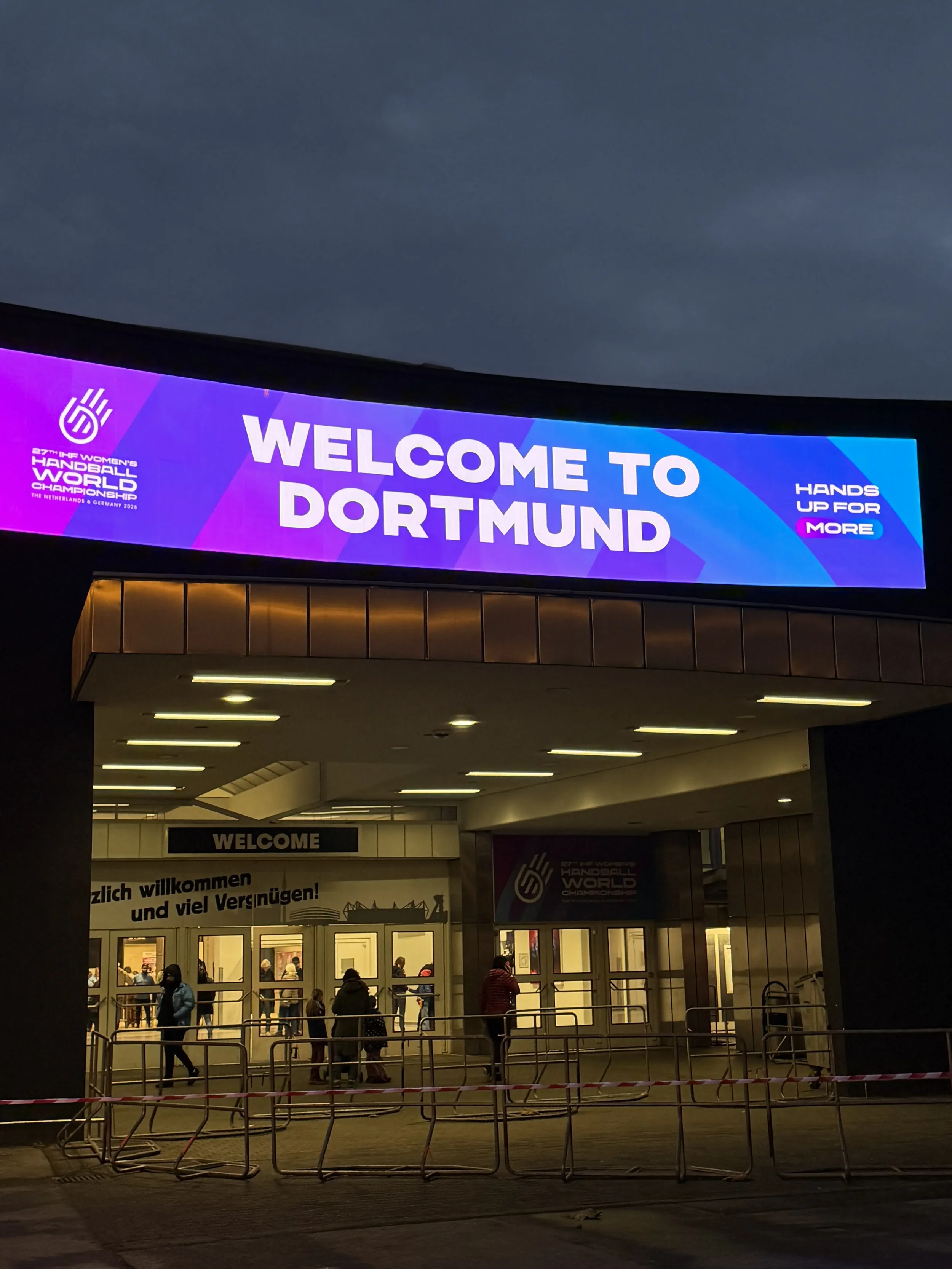 Eingangsbereich der Westfallenhalle Dortmund. Auf einem violetten Banner steht in weißer Schrift: Welcome to Dortmund. Links ist das Logo der Hanball-WM der Frauen zu sehen.