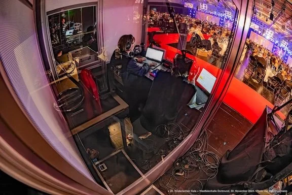 Blick von hinten in eine Dolmetschkabine mit zwei Dolmetscherinnen und Technik.