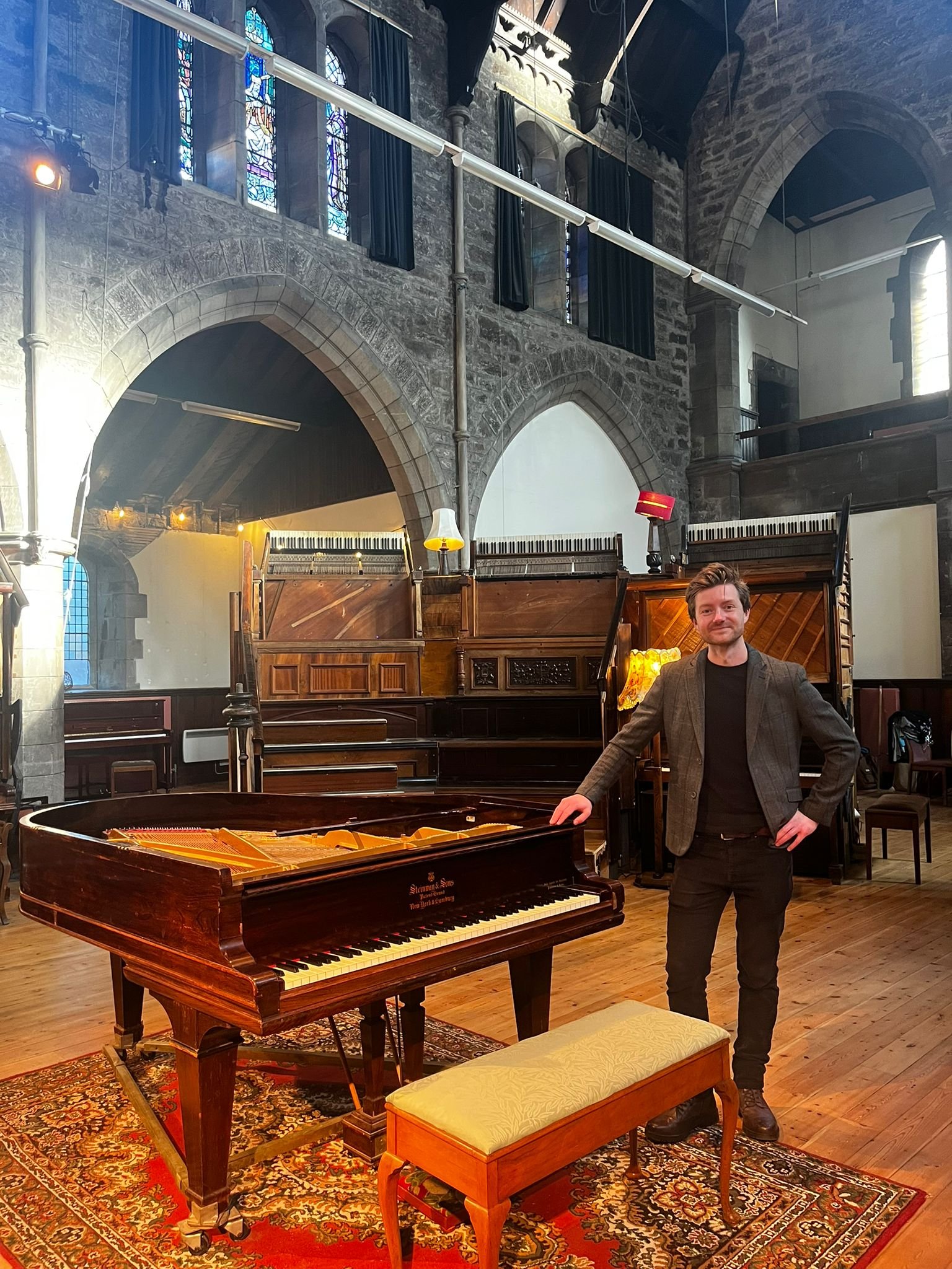 Nick Lauener, a piano teacher in Edinburgh stands by grand piano inviting you for beginner piano lessons, intermediate piano lessons or advanced piano lessons in Edinburgh.