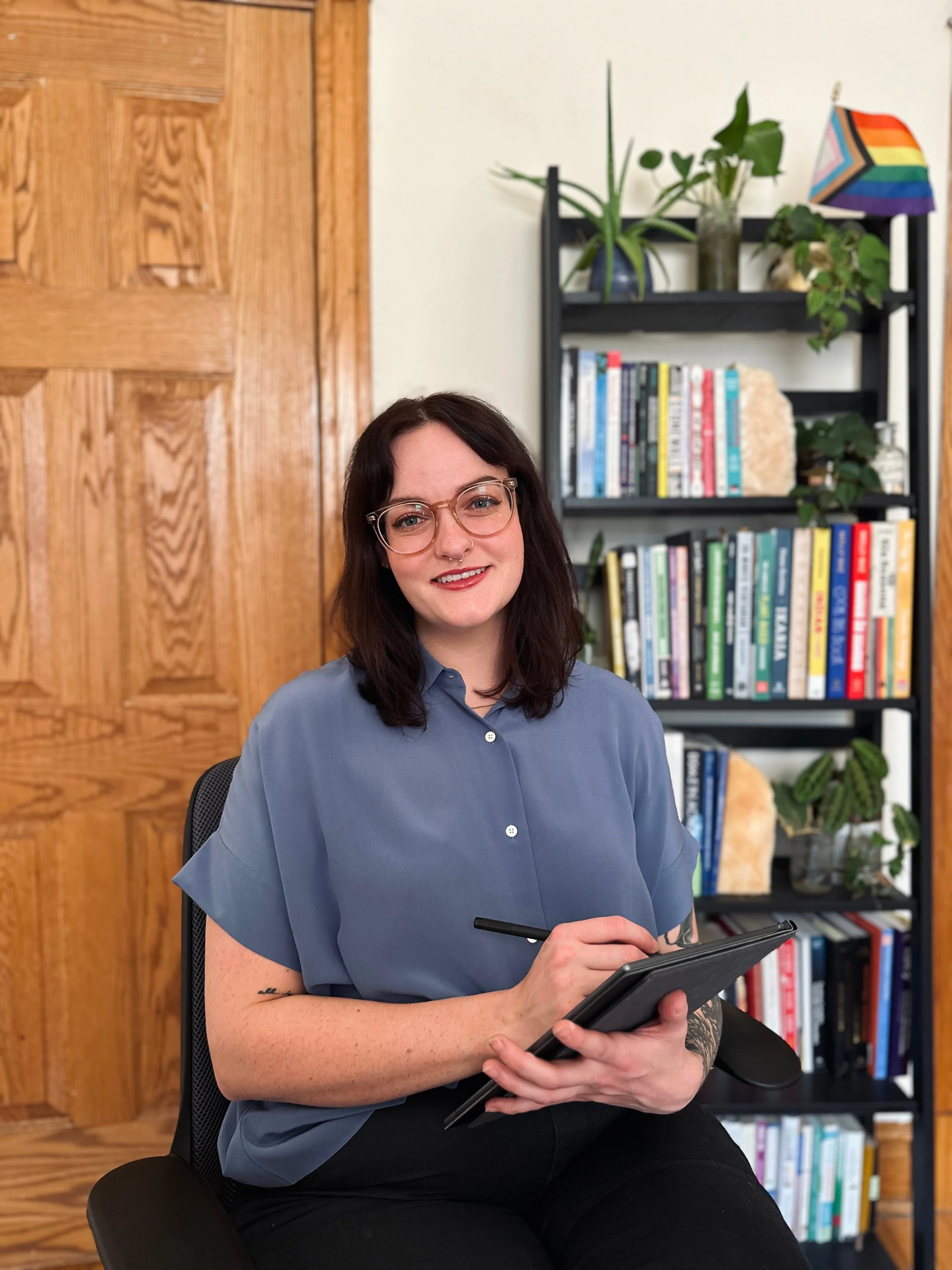 Sex therapist, Marlee, wears a blue button up shirt as they take notes from a therapy session