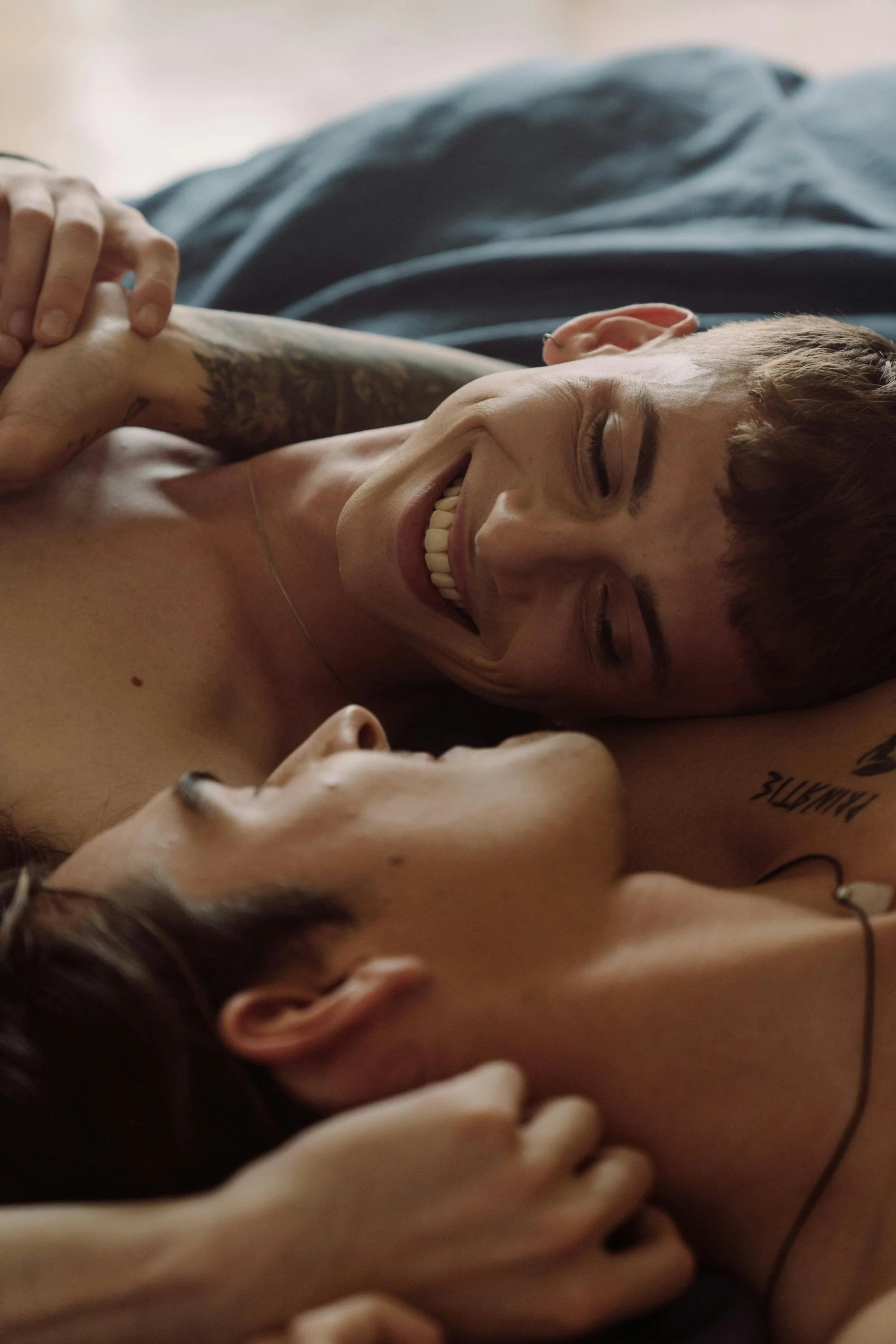Two queer people lying close and smiling, sharing a moment of intimacy and connection. This image reflects the joy, safety, and emotional support that LGBTQ+ affirming therapy can offer.