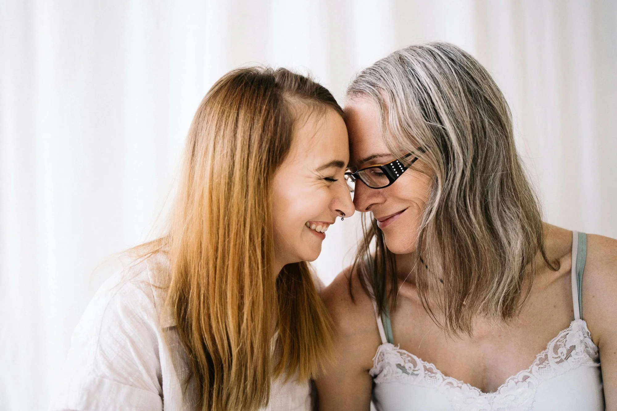Two women with foreheads touching, smiling and showing affection in a close-up shot.