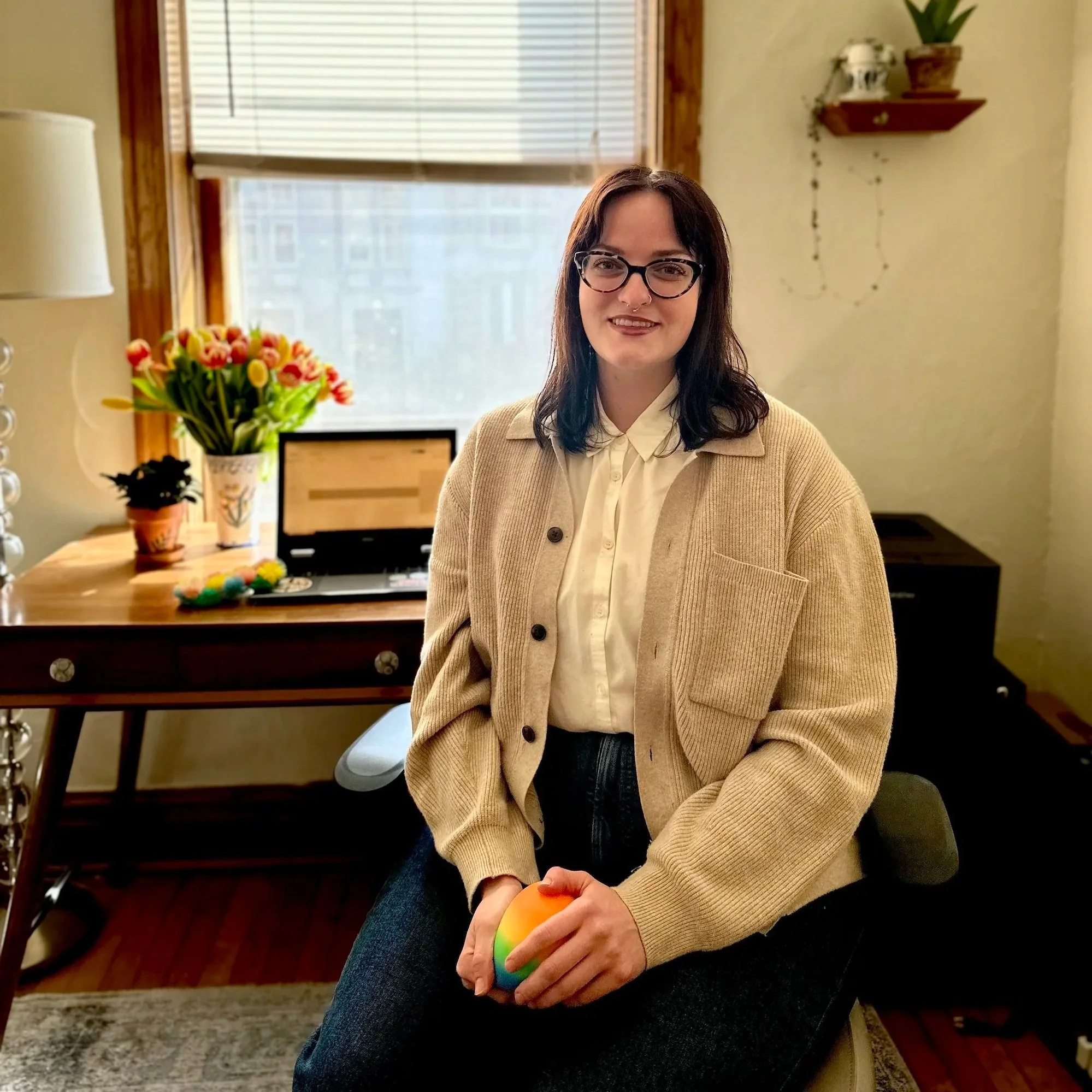 Marlee Gebhard, LCSW seated at a desk in her therapy office holding a rainbow fidget toy.