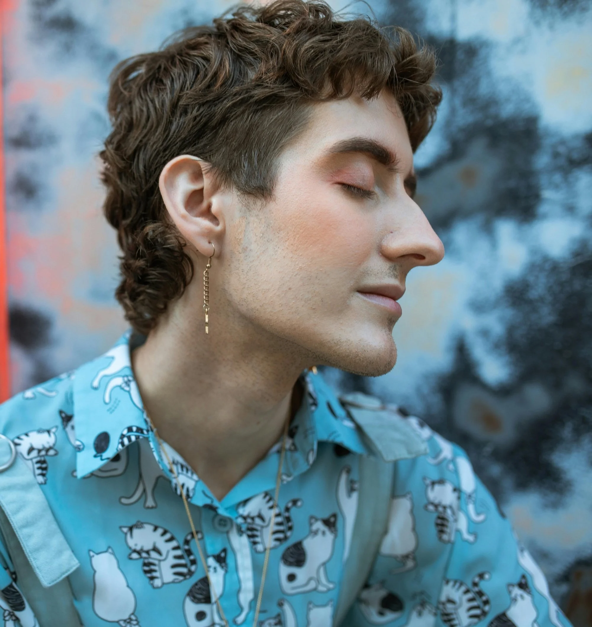 Person with short, curly hair and a cat print button up, looking at peace in themselves