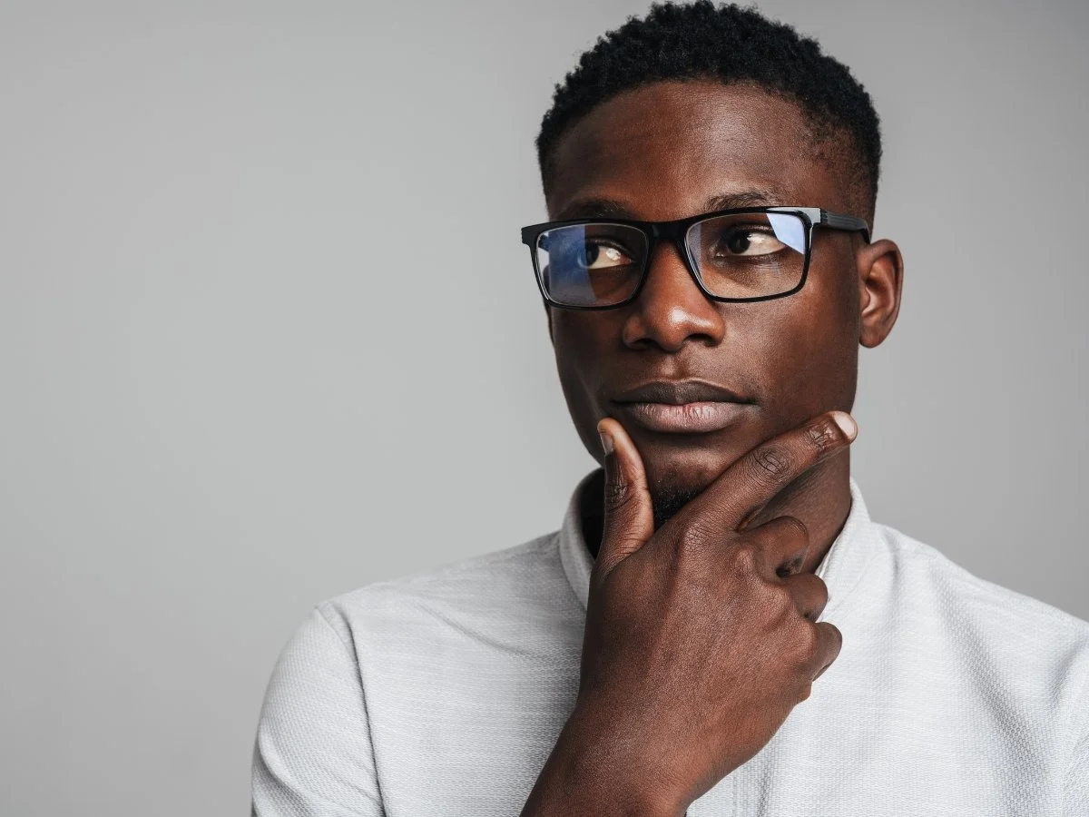 Thoughtful man wearing glasses with his hand on his chin, looking off to the side in deep reflection and self-inquiry.