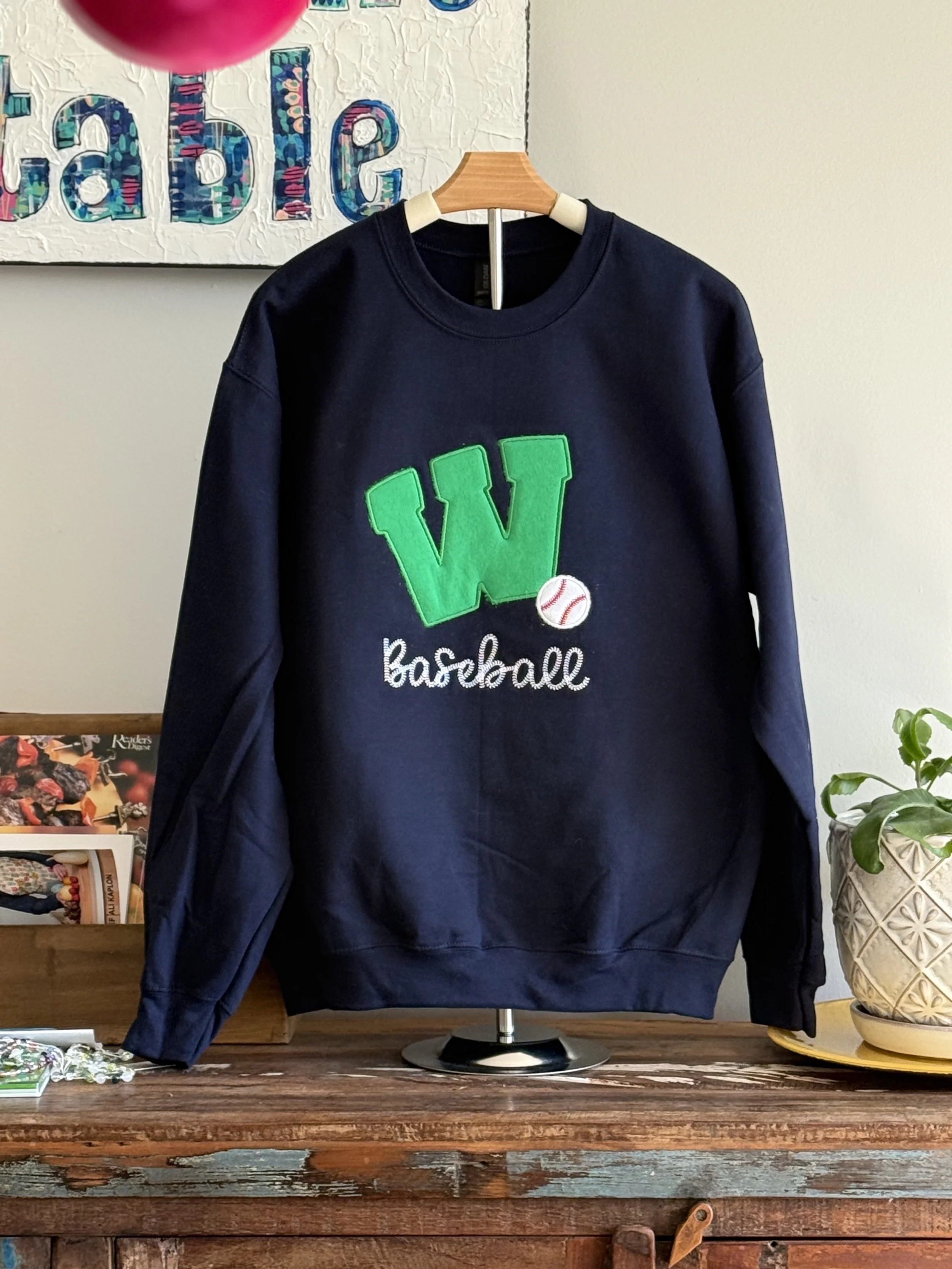 Navy crew sweatshirt with green Weddington W and baseball appliques with the word Baseball written in a stitch script in whtie underneath.