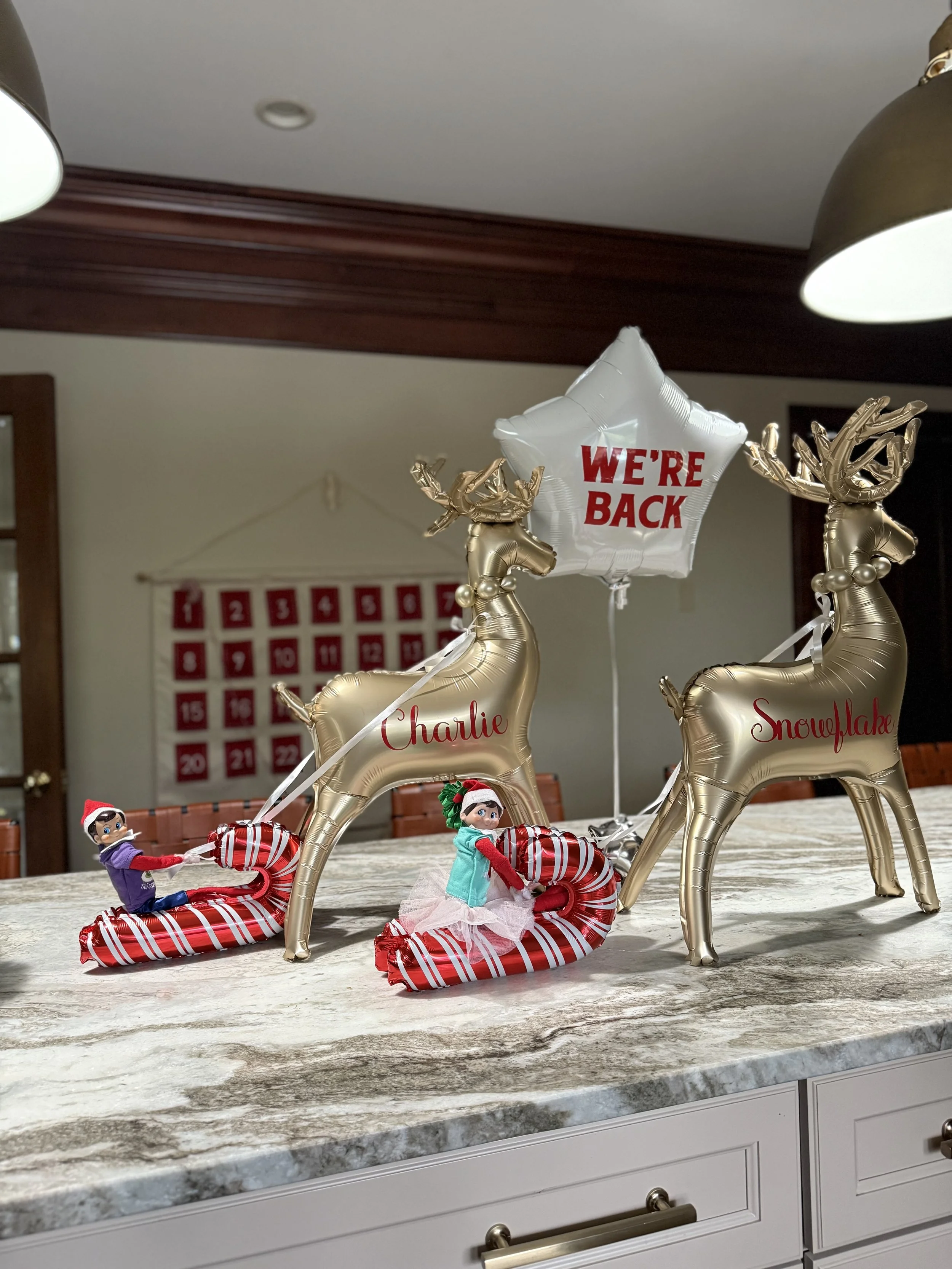 two silver deer balloons on a kitchen counter; elf dolls riding on candy can balloon sleighs 