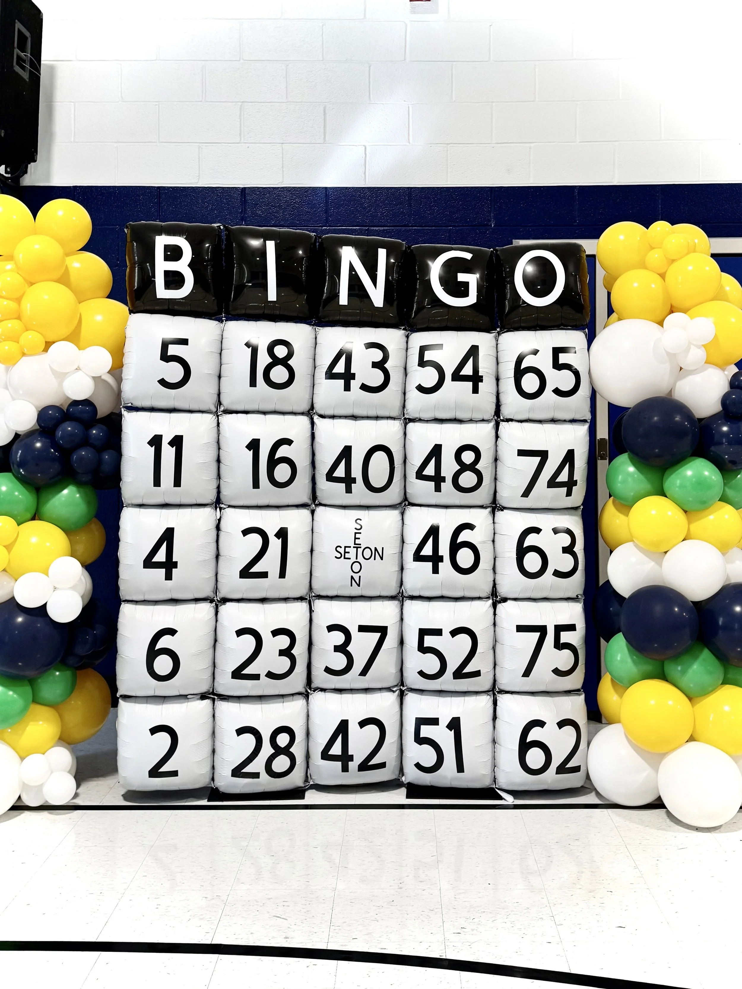 large six foot bingo card made out of square balloons; yellow, white, blue, and green balloons are on each side.