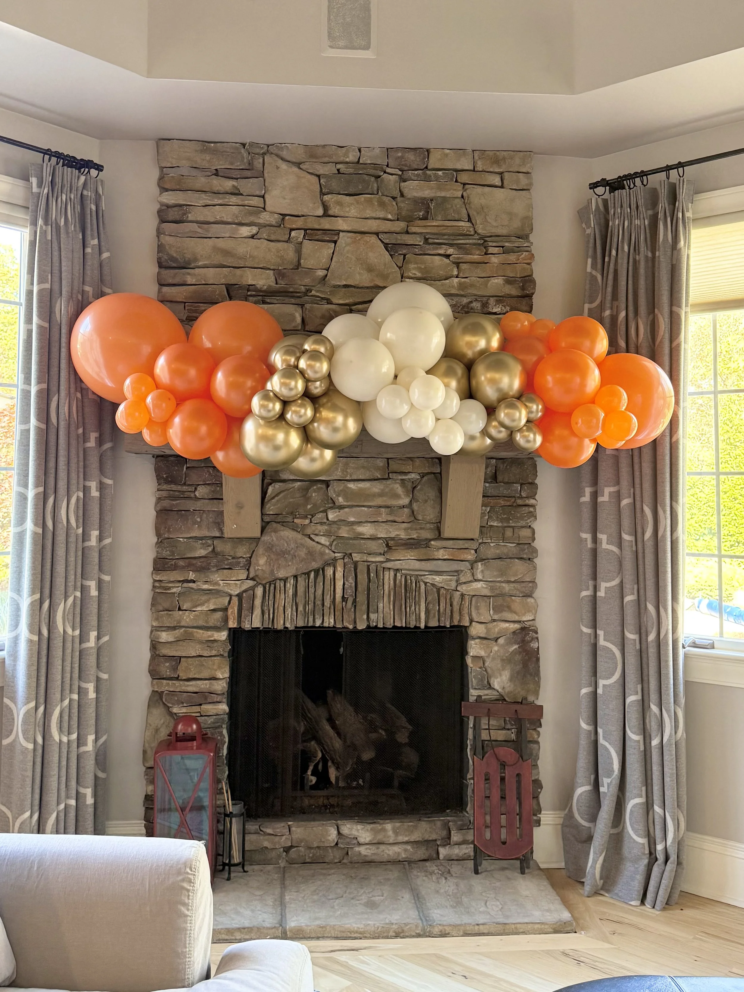 orange, gold and white balloon garland hung over a fireplace