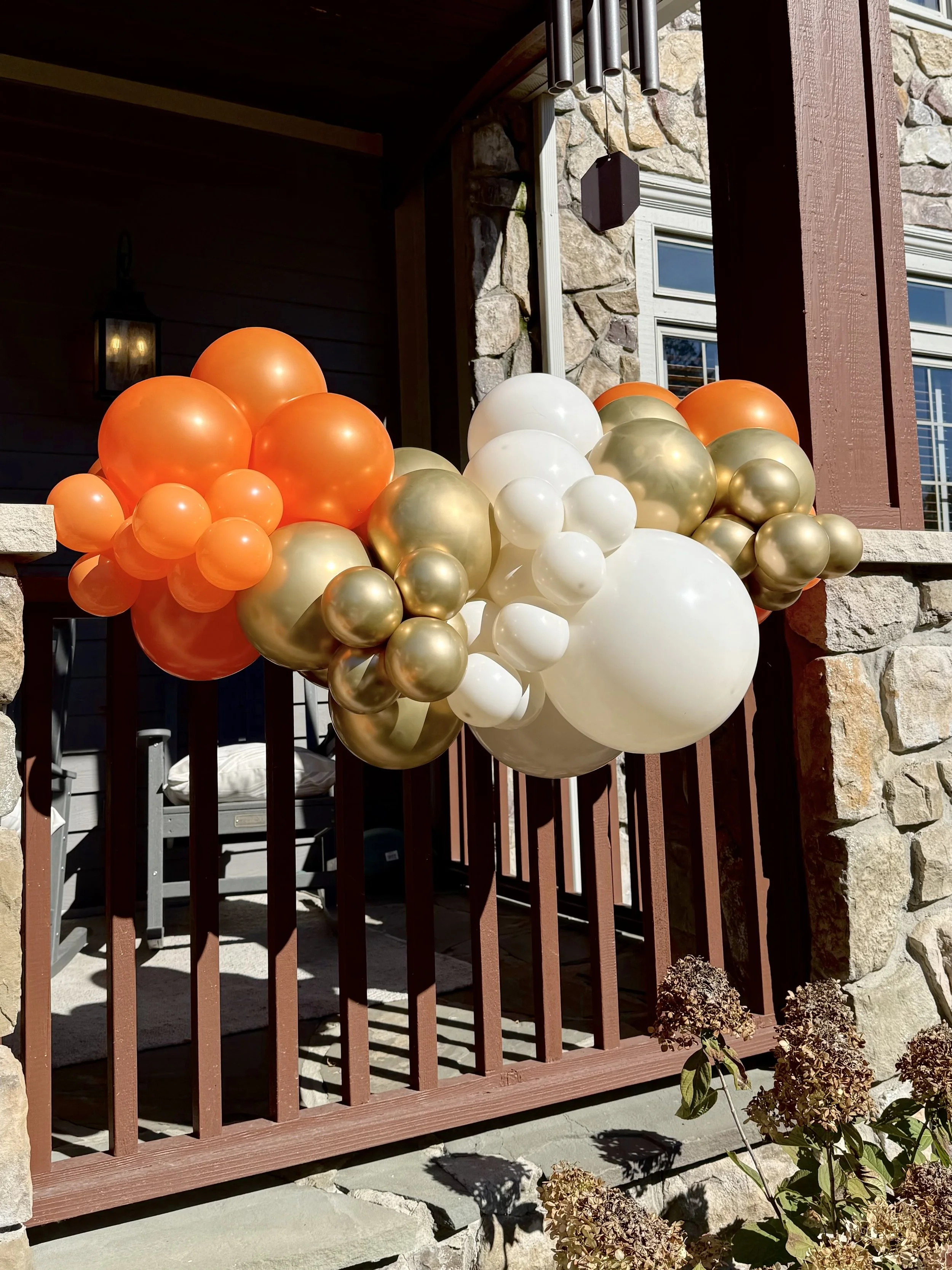 front porch with orange, white, and gold balloons attached to railing