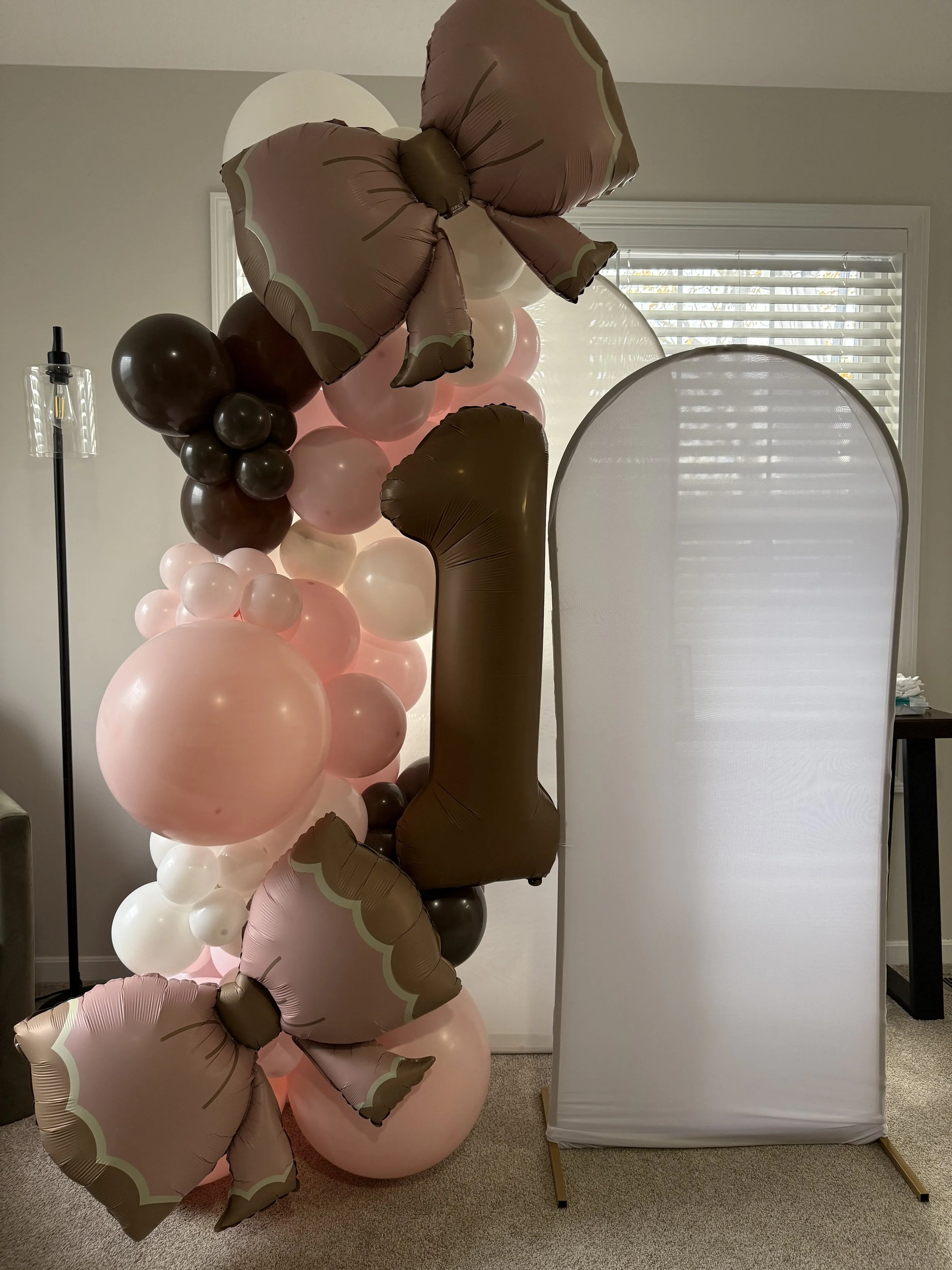 brown number one balloon with pink, white and brown balloons; two arches with white spandex covers
