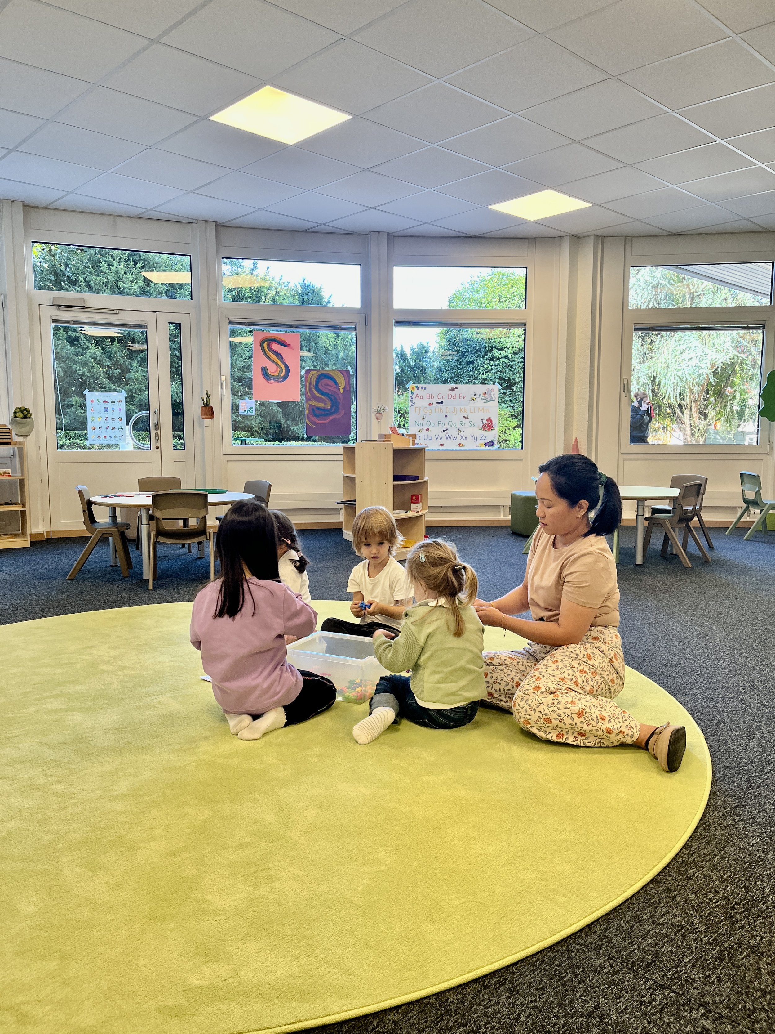 Salle de classe préscolaire à l’École Eden avec grandes fenêtres, espace de regroupement, matériel éducatif coloré et activité encadrée favorisant apprentissage et échanges.