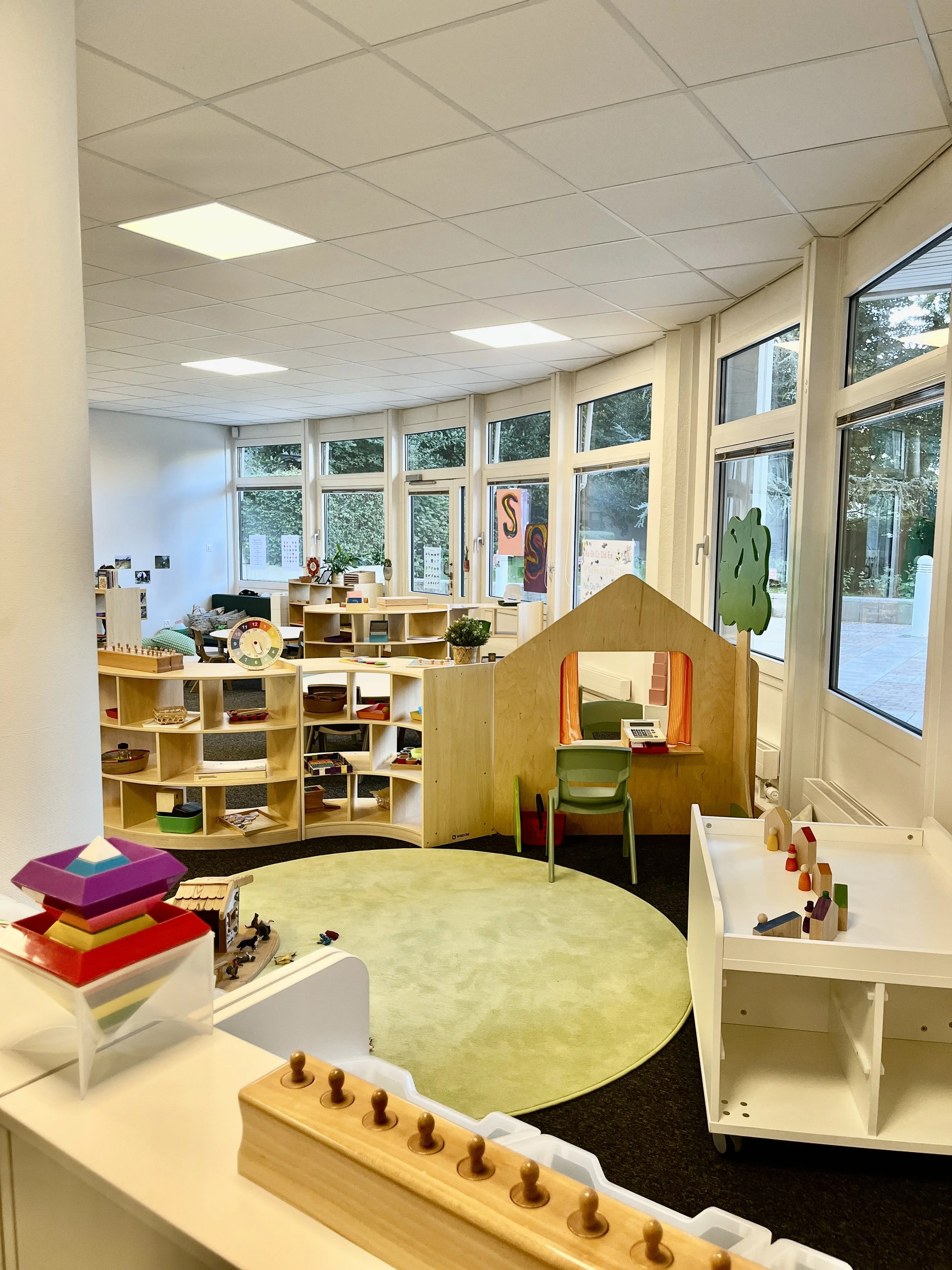 Salle de classe et espace jeux à l’École Eden avec jouets en bois, grandes fenêtres lumineuses, étagères organisées et environnement chaleureux favorisant l’apprentissage.