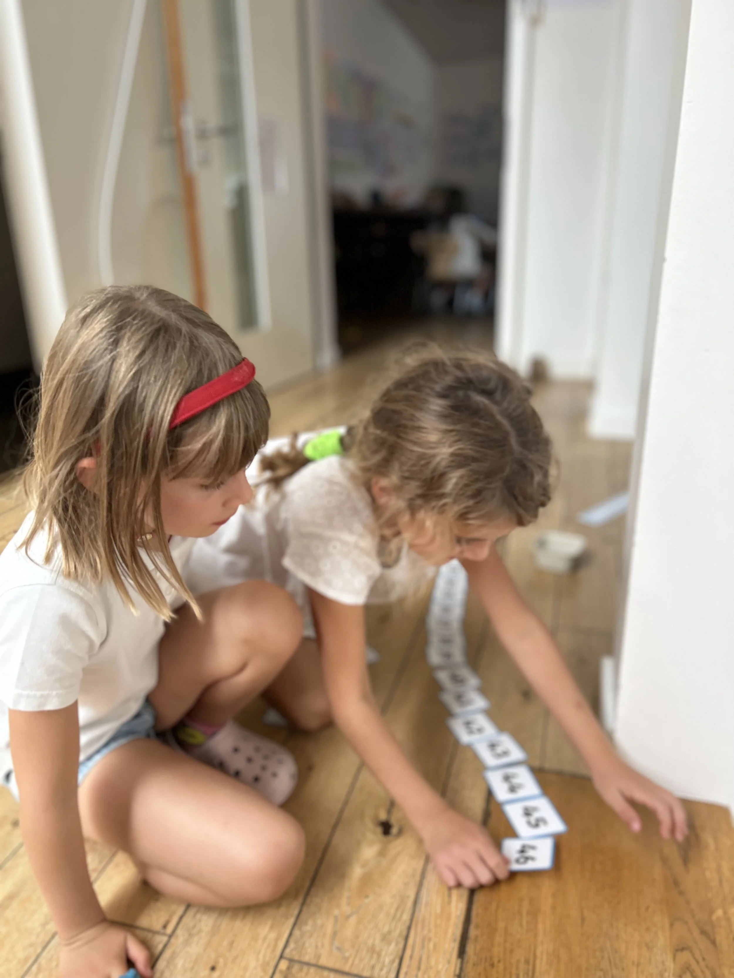 Two students at Ecole Eden in Veyrier, Geneva, are playing with numbered cards, developing logical thinking, math skills, and learning through play in an educational setting.