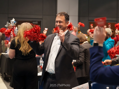 AnMed executive at the 2025 Live2Lead in Anderson, holding a red pompom and cow bell decoration smiling among a crowd enjoying the event.