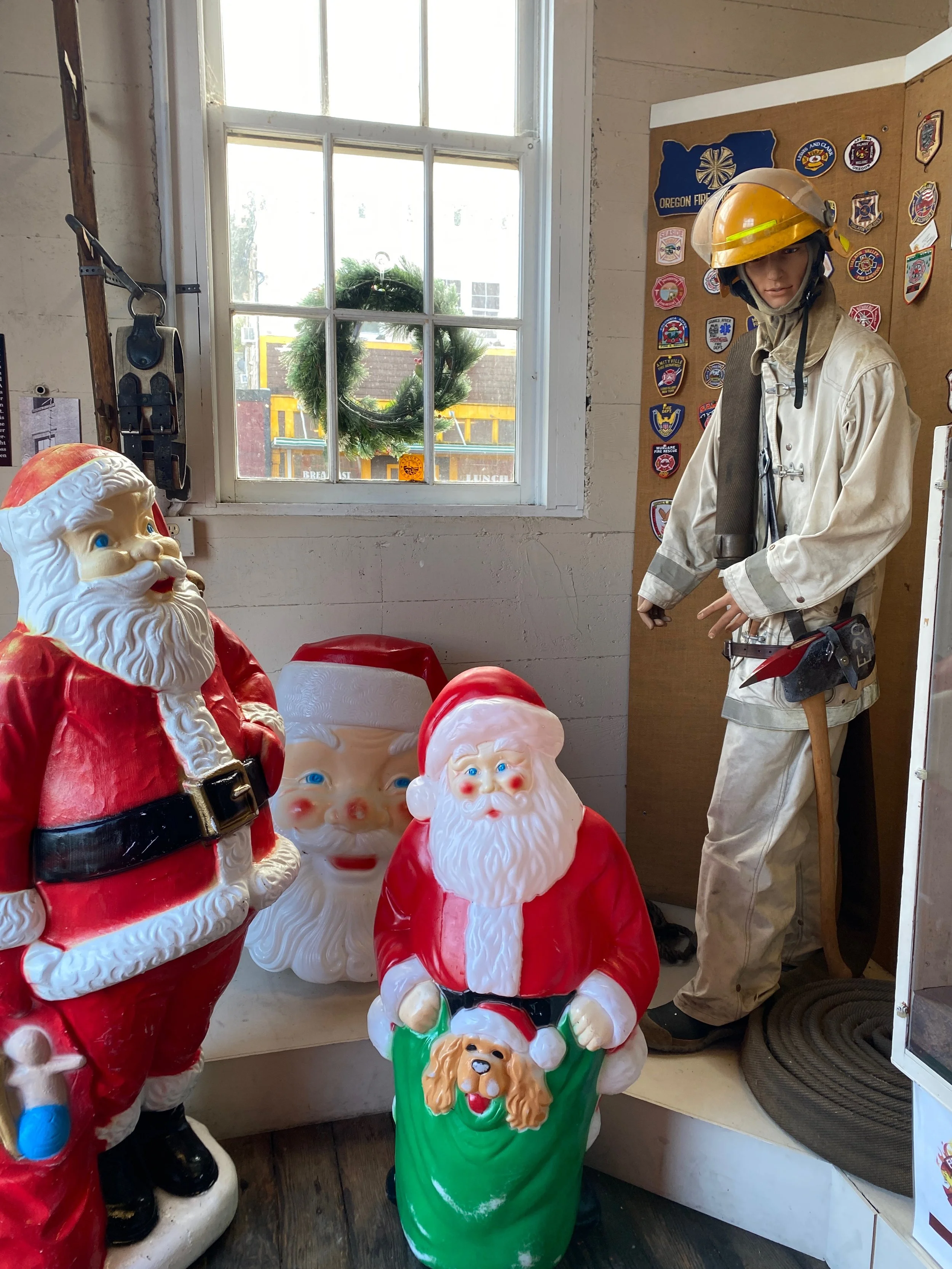 Christmas decorations including Santa Claus figures, a Christmas wreath outside the window, and a firefighter mannequin with a helmet inside a store decorated for the holidays.