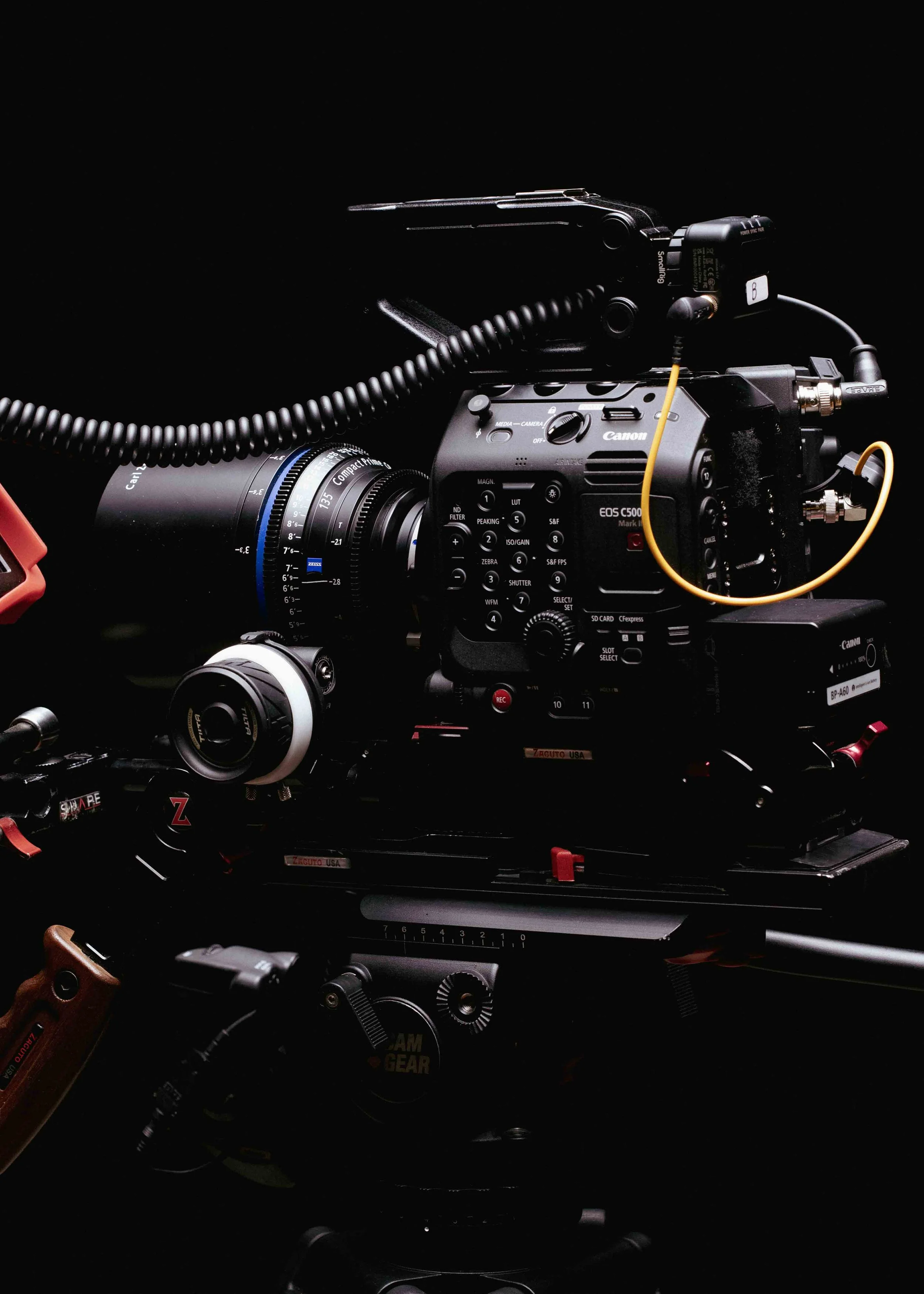 Close-up of a professional video camera on a dolly, with a lens, microphone, and various controls, set against a dark background.