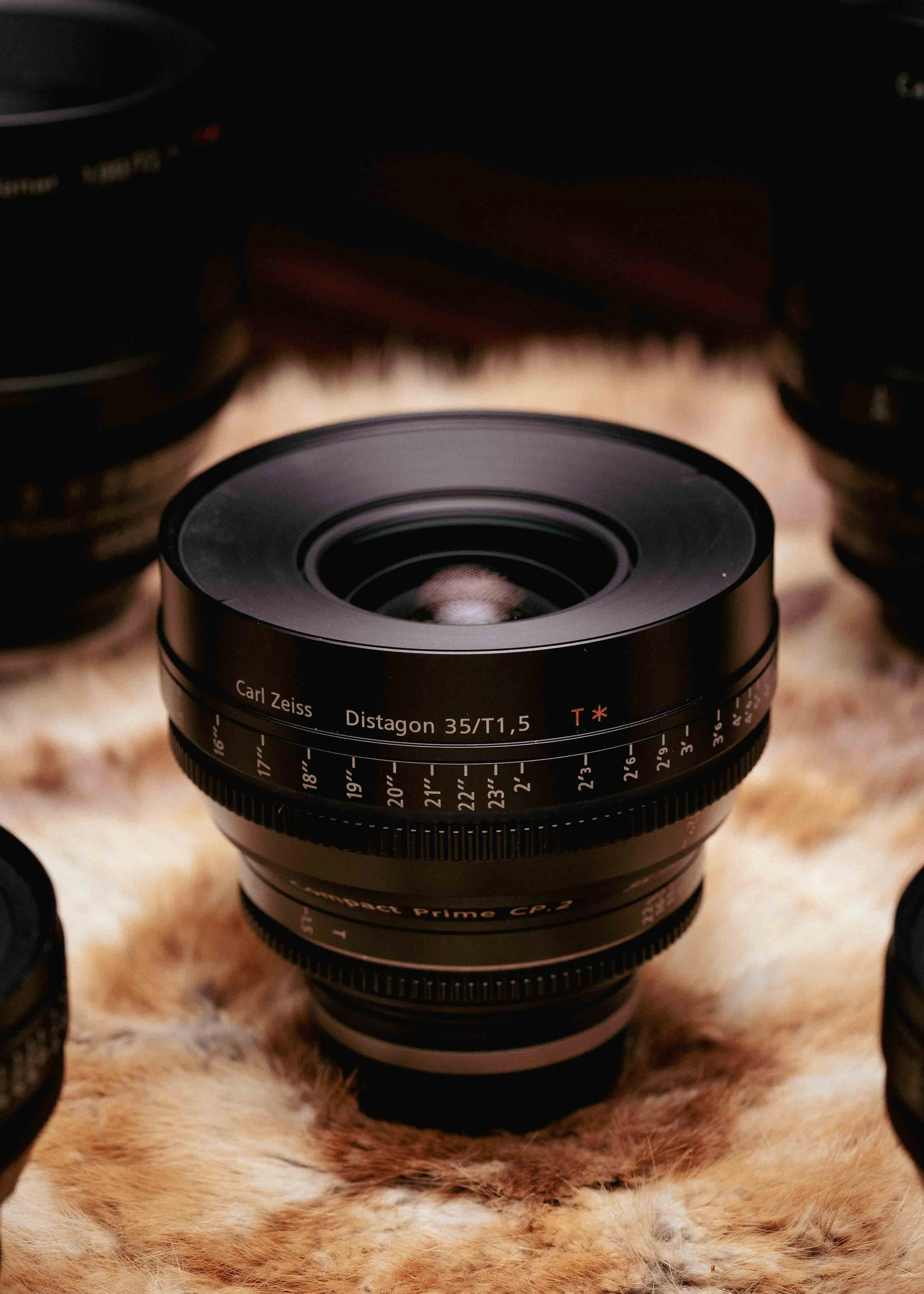 Close-up of a Carl Zeiss Distagon 35mm f/1.4 camera lens on a furry surface with other camera lenses partially visible around it.