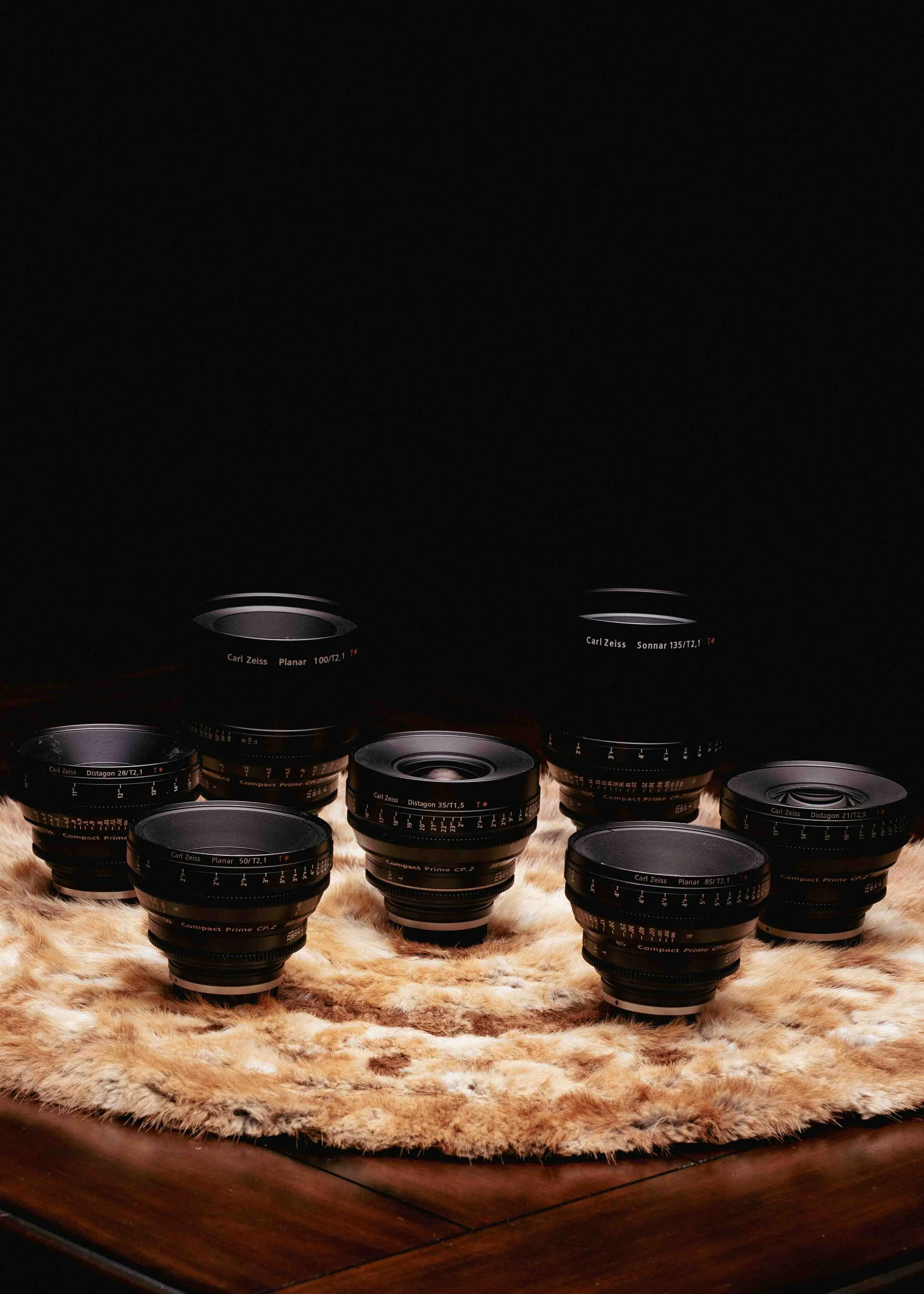 A collection of camera lenses arranged on a furry surface against a black background.