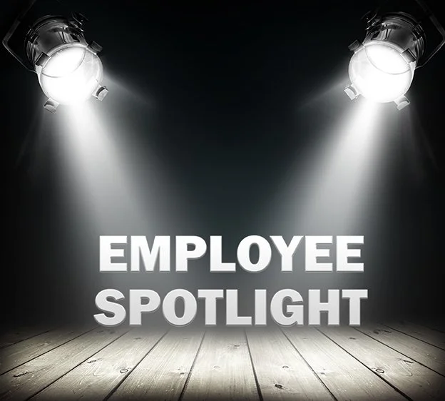 Lights aimed at a sign reading "Staff Spotlight Series" in neon-style lettering with a dark background.