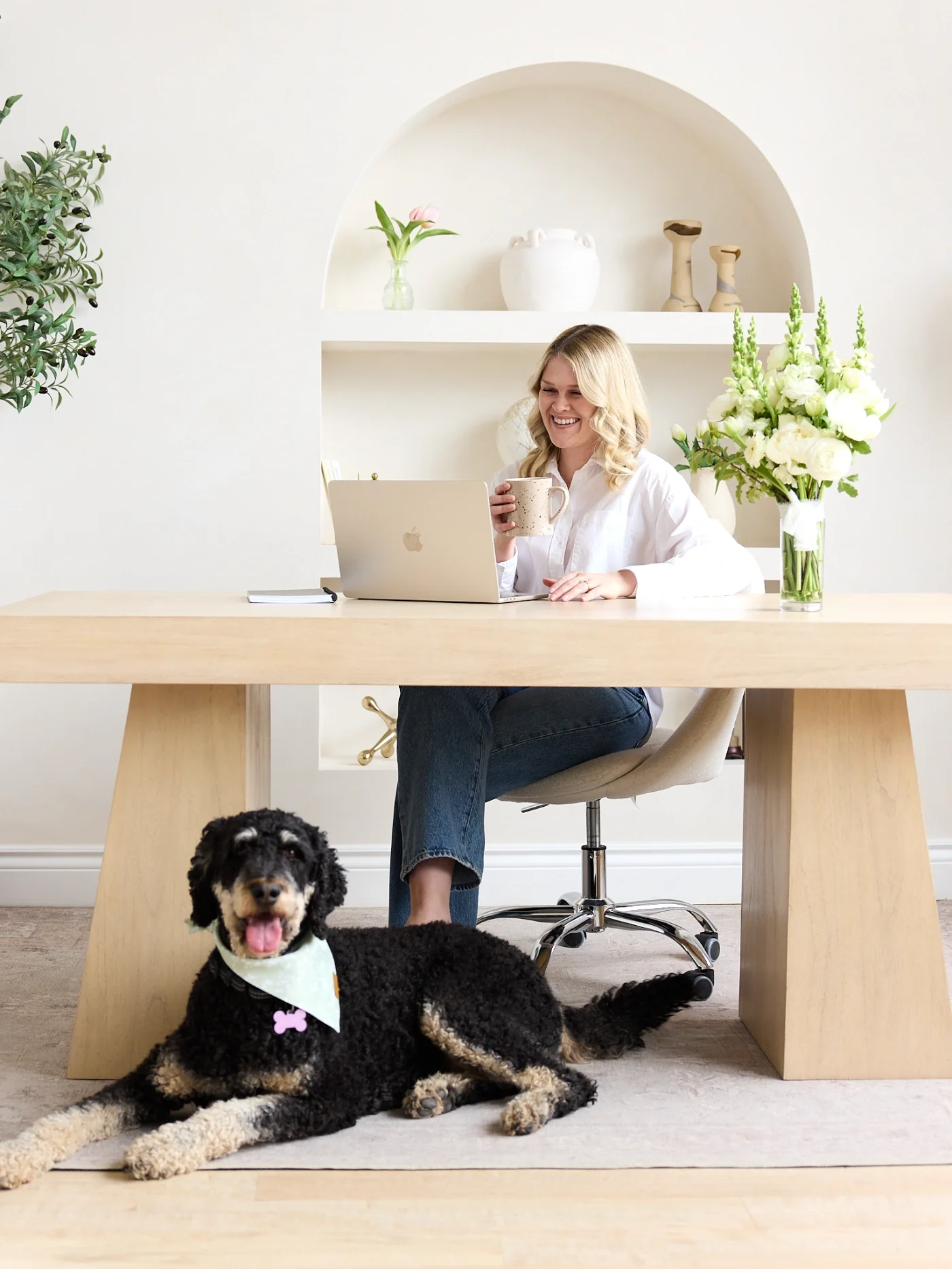 Katelyn of Ripple Effect Psychotherapy in Hamilton, Ontario sitting at a wooden desk, smiling and holding a coffee mug, using a silver laptop.