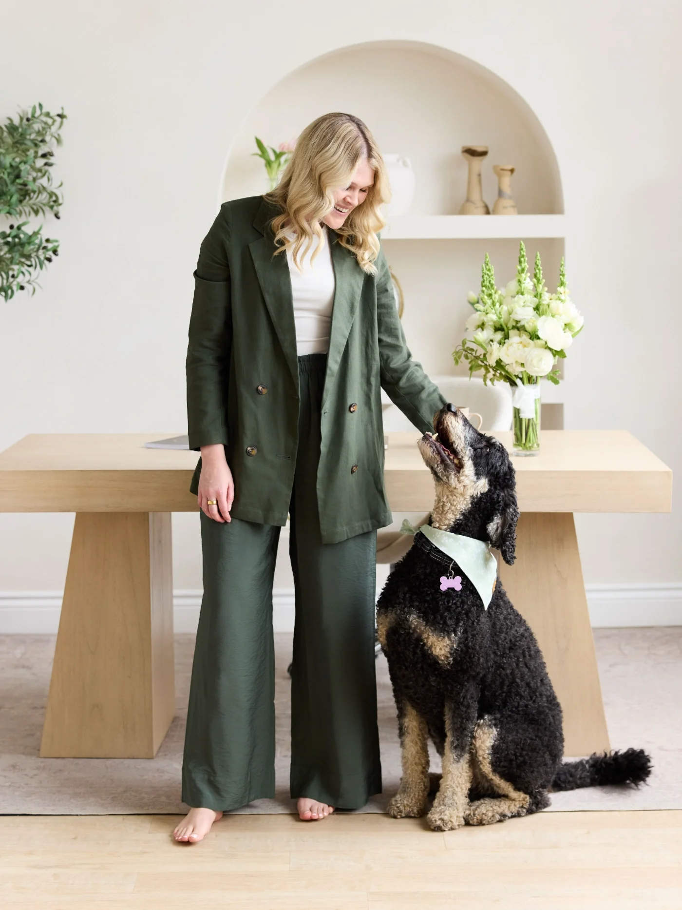 Katelyn a ripple effect therapist leaning against a desk, with flowers, and her dog looking up to her.