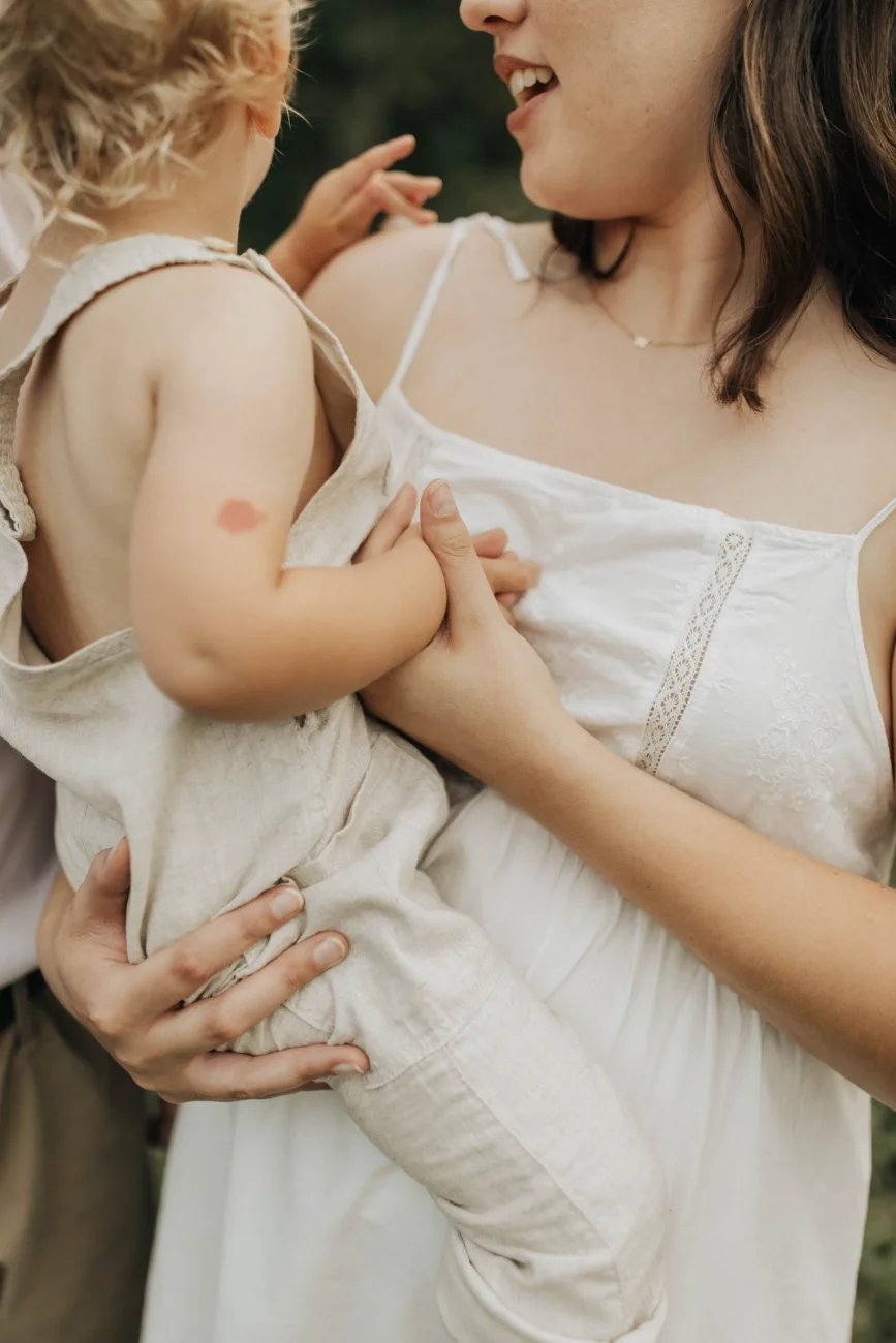 A woman holding a young child outdoors, close-up of their torsos and faces, both smiling.
